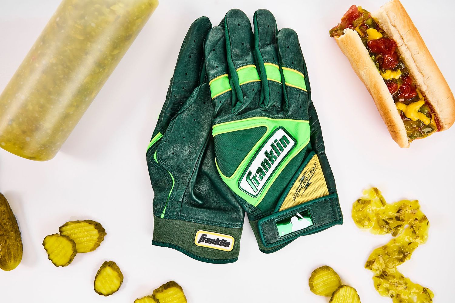Green gardening gloves and pickles scattered on white background with soft shadows.