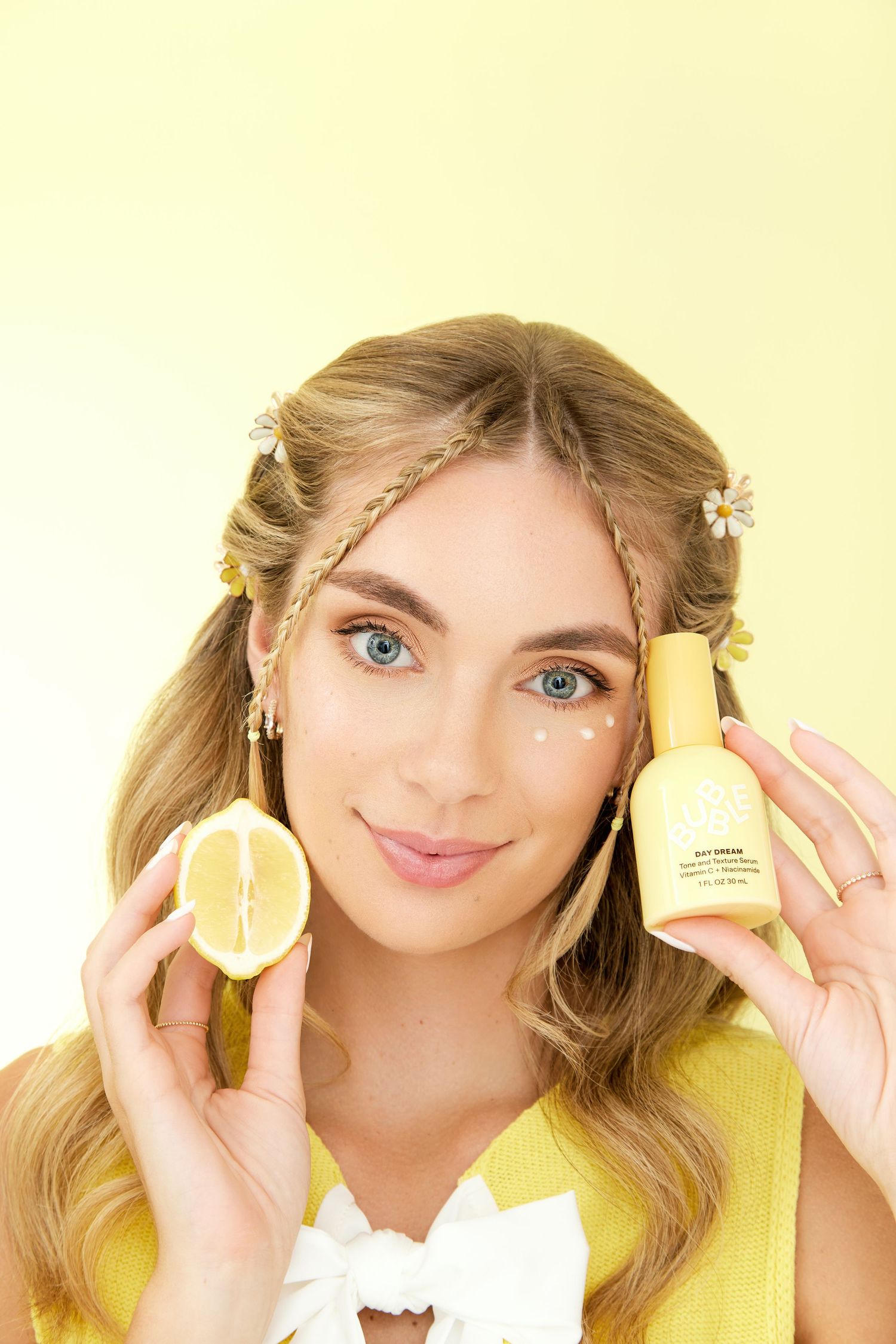 A person with blonde hair holds up lemon halves against a yellow background in a playful series of poses.