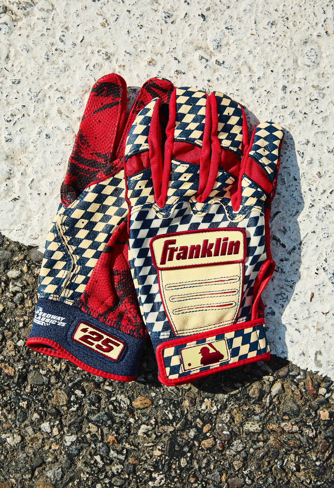 Red and black Franklin baseball batting gloves with checkered pattern design shown from different angles on gravel surface.