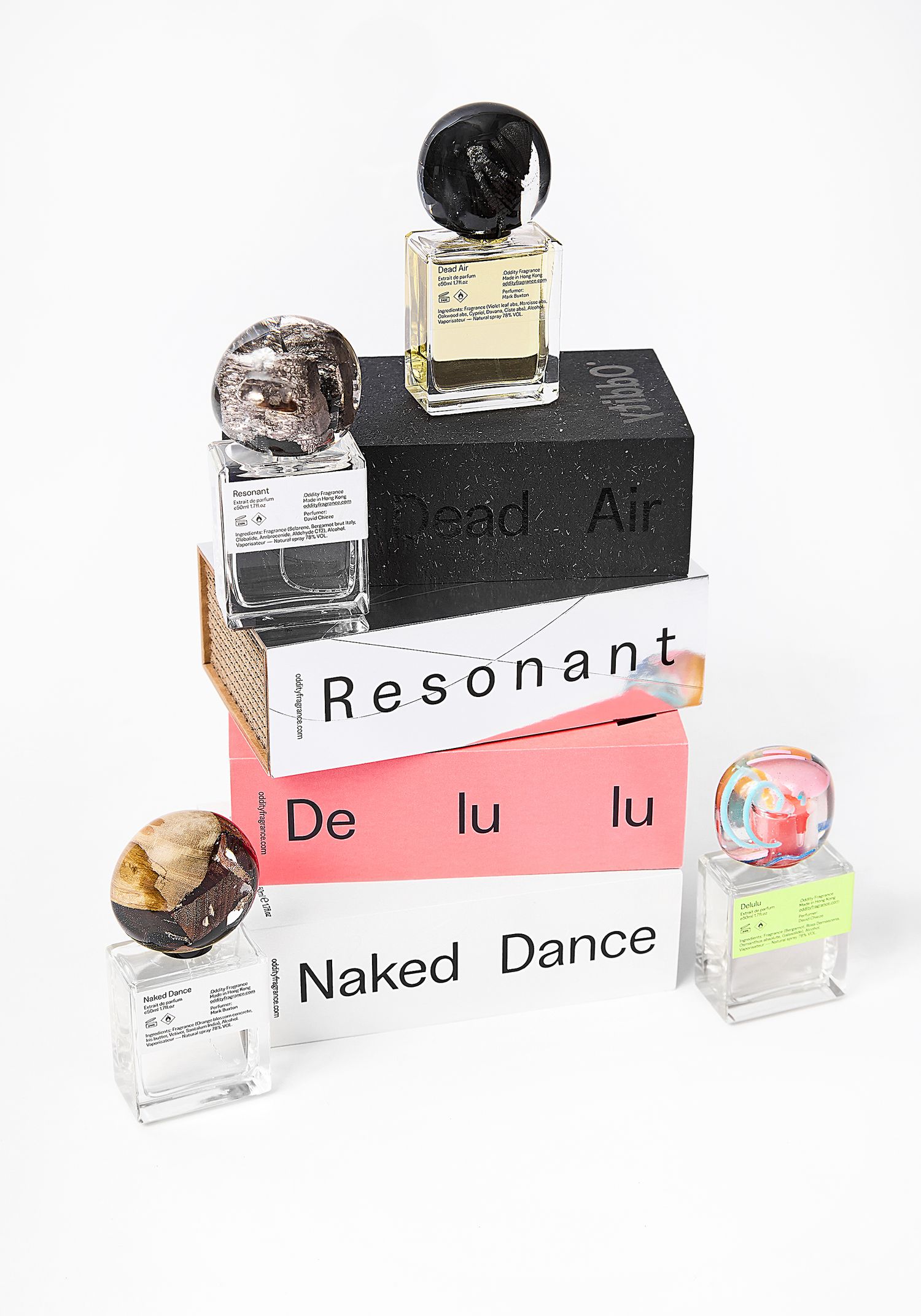 Four perfume bottles with colorful marble-like caps stacked atop boxes labeled Dead Air, Resonant, Delulu and Naked Dance.