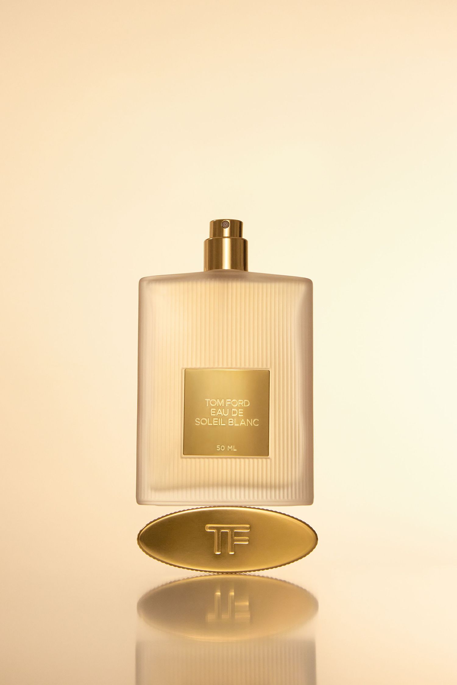 Tom Ford Eau de Soleil Blanc fragrance bottle with gold label and TF logo medallion on warm beige background.