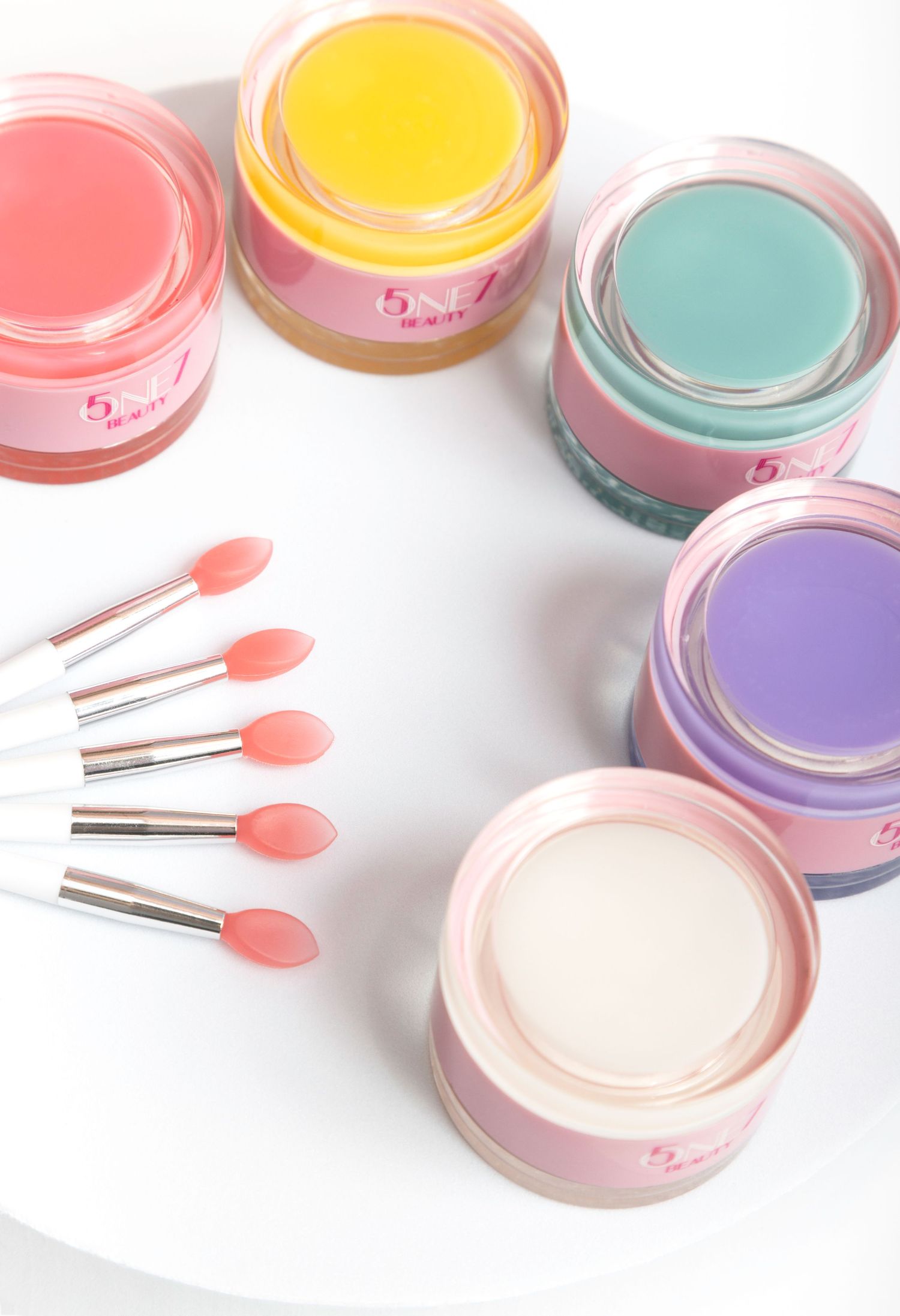 Colorful pastel beauty blushes and compacts arranged in a diagonal line with pink heart-shaped applicators.