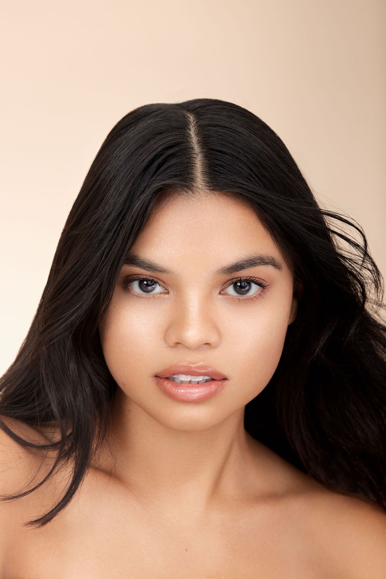 Beauty portrait with long flowing dark hair against neutral beige background.