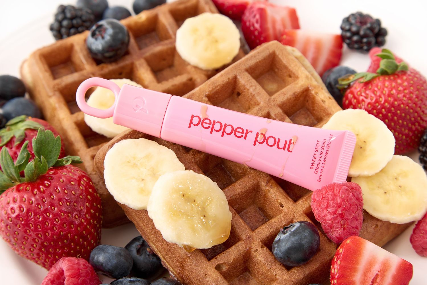 Pepper Pout lip gloss tube displayed on waffles surrounded by fresh strawberries, blueberries, and banana slices.