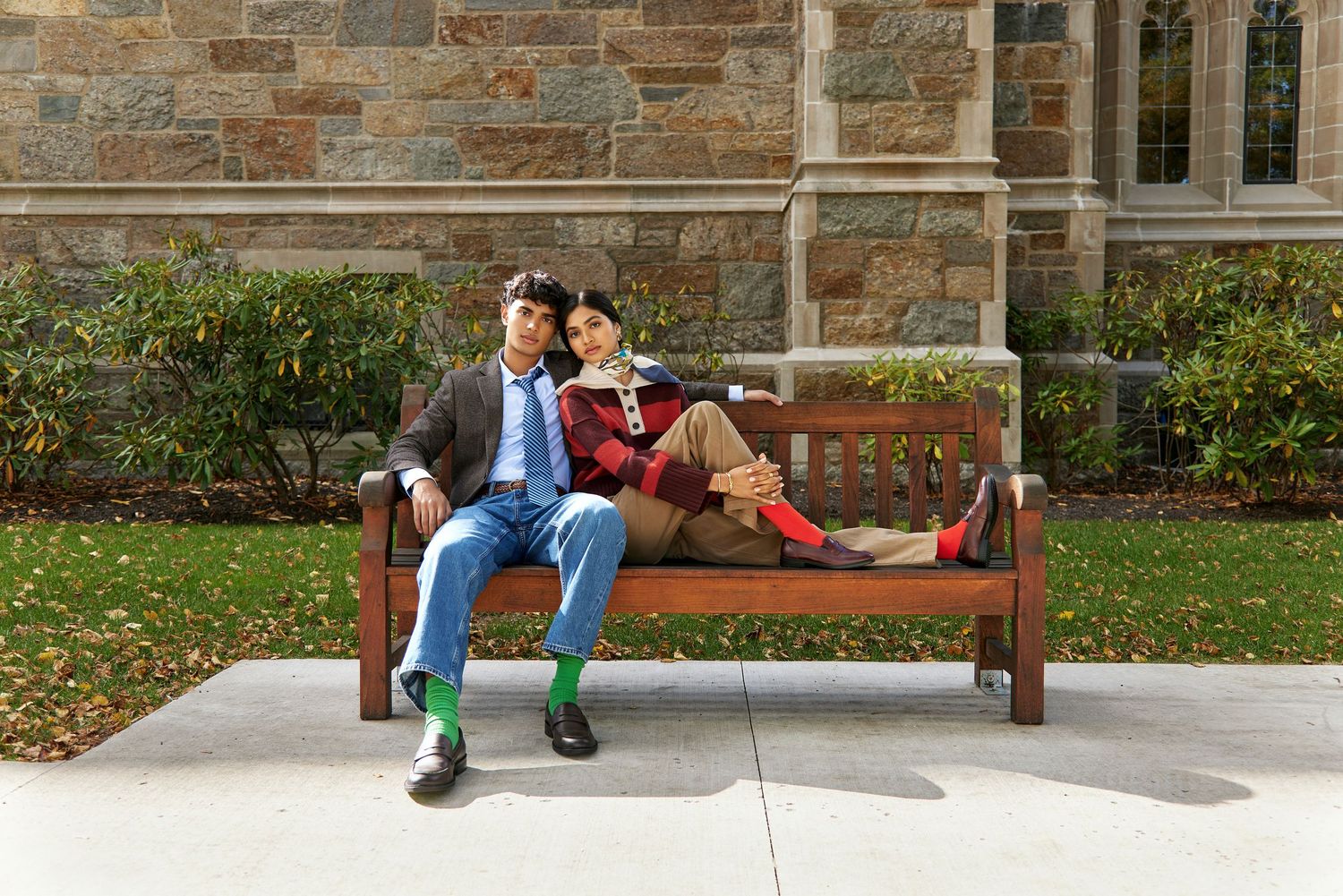 Students relax on wooden benches outside a stone building on a university campus.