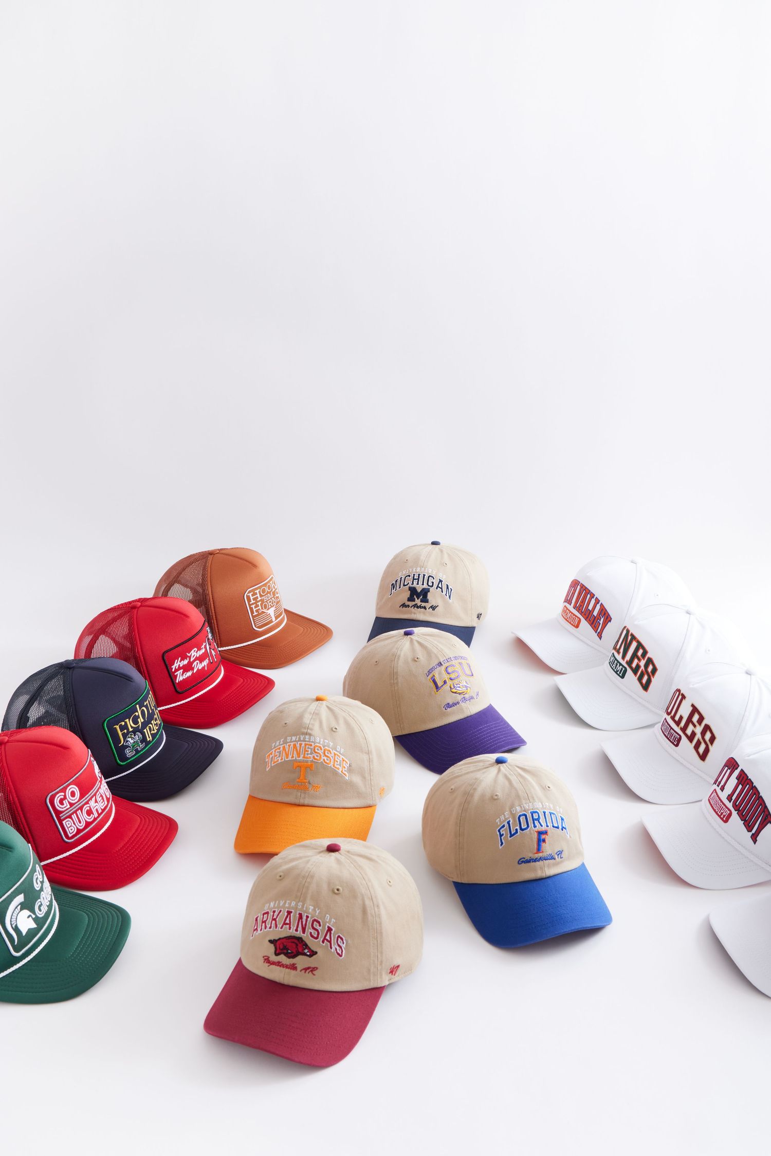 A collection of vintage and modern sports team baseball caps in various colors arranged in a row on white background.