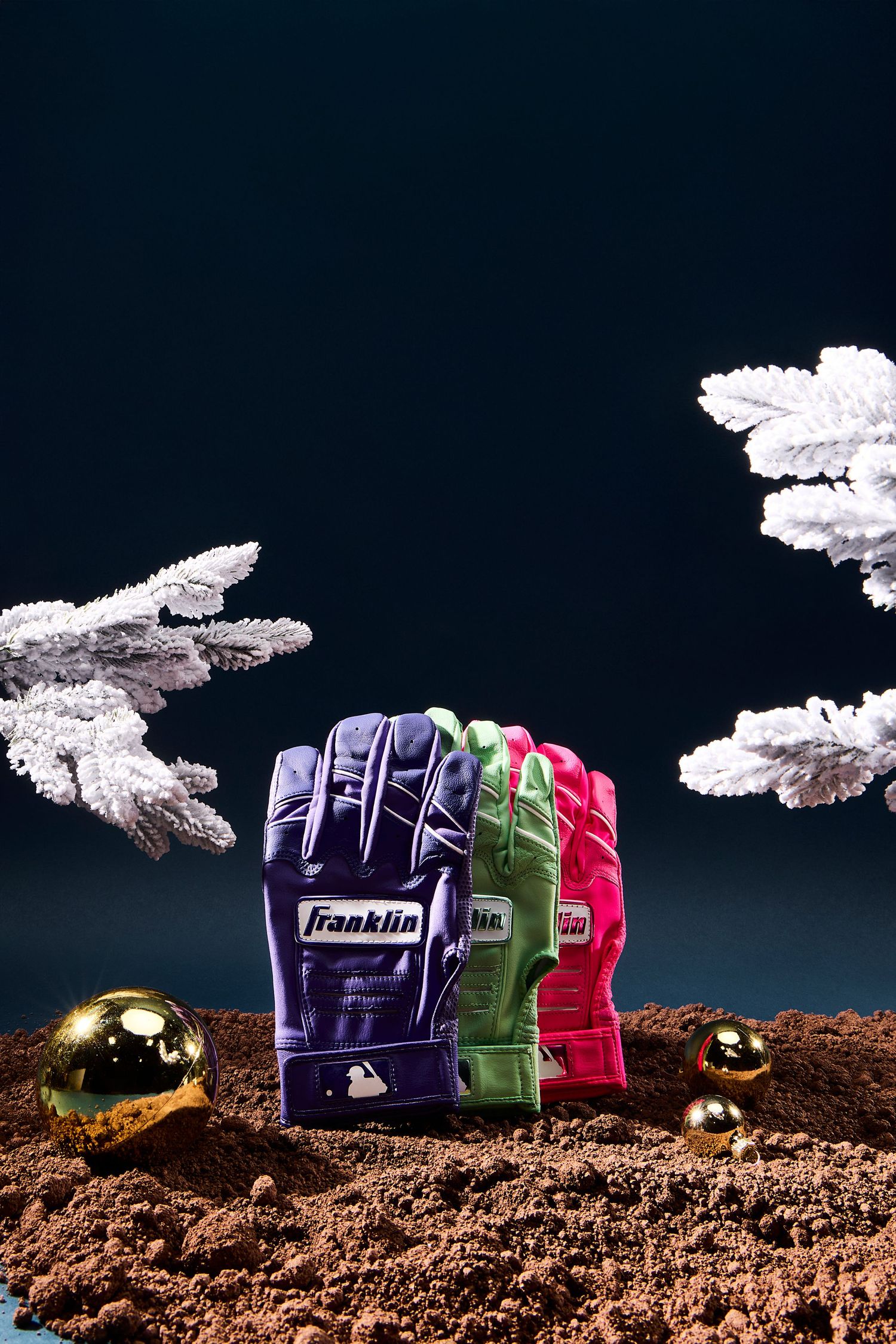 Three colorful baseball gloves arranged on dirt ground against a dark background with white clouds and dramatic lighting.