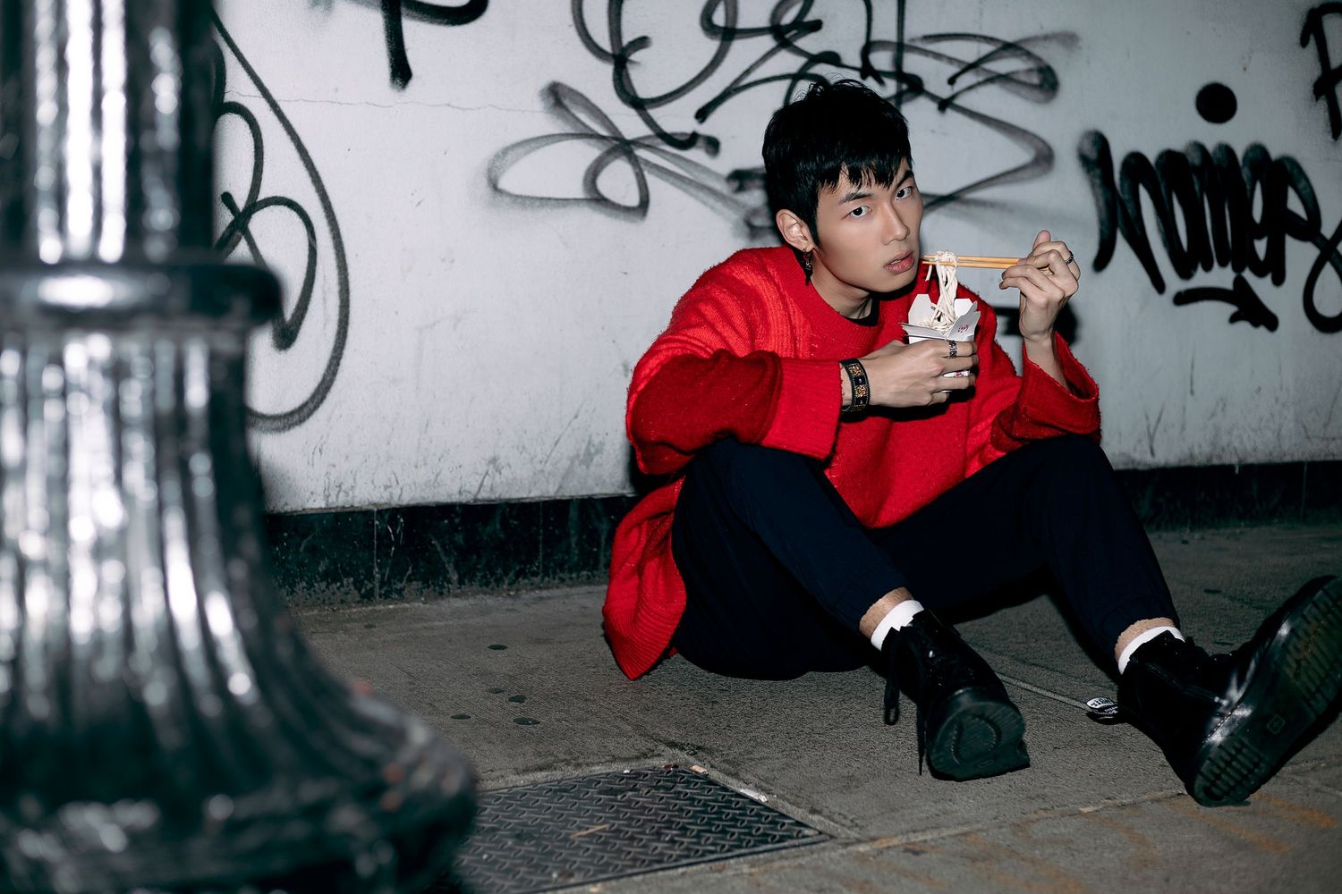 A skateboarder in a red hoodie performs tricks in an urban tunnel covered with graffiti.