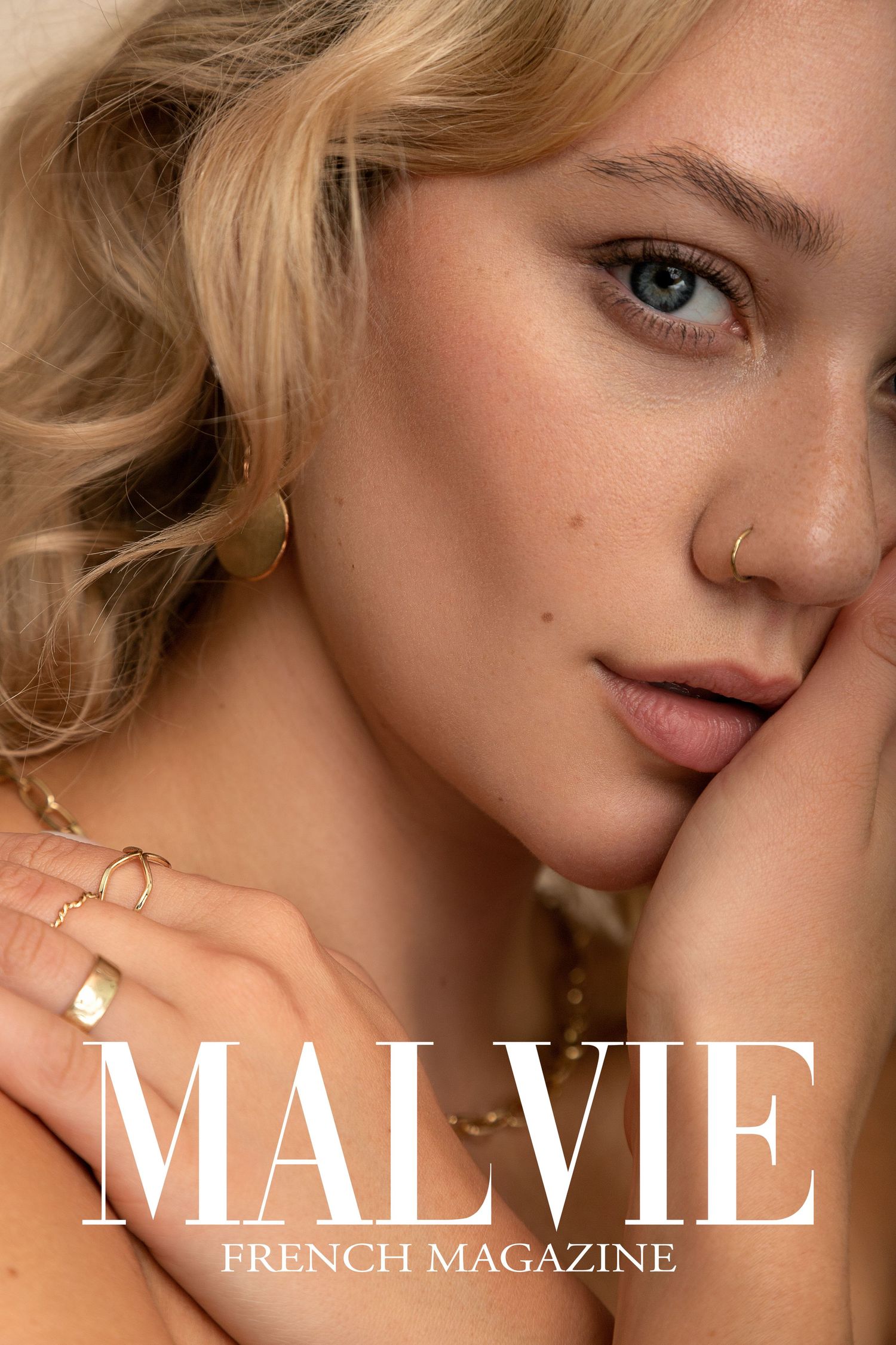 Fashion magazine cover design featuring soft lighting, blonde hair, and delicate gold jewelry against a neutral background.