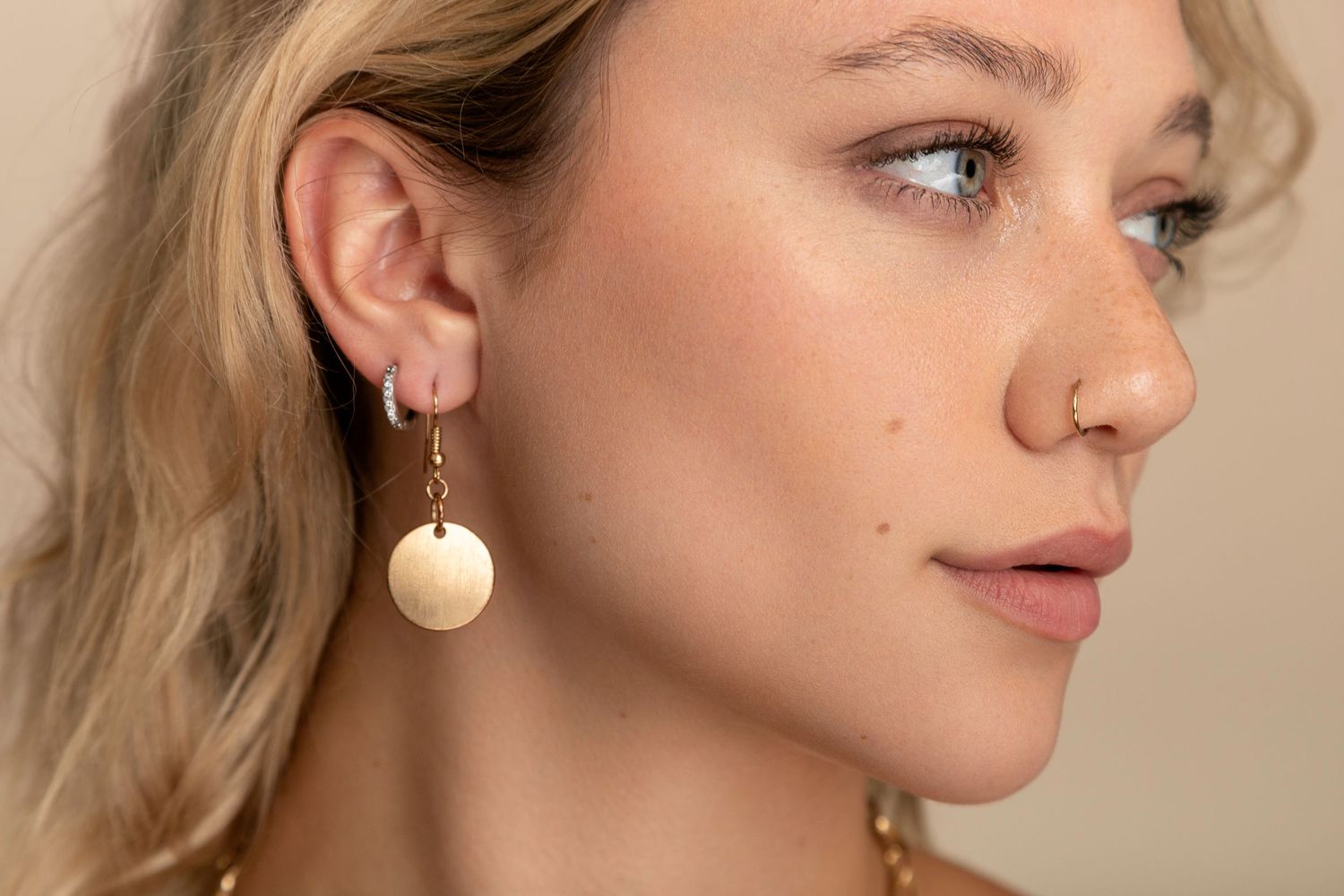 Side profile view showing a gold disc earring on a light background.