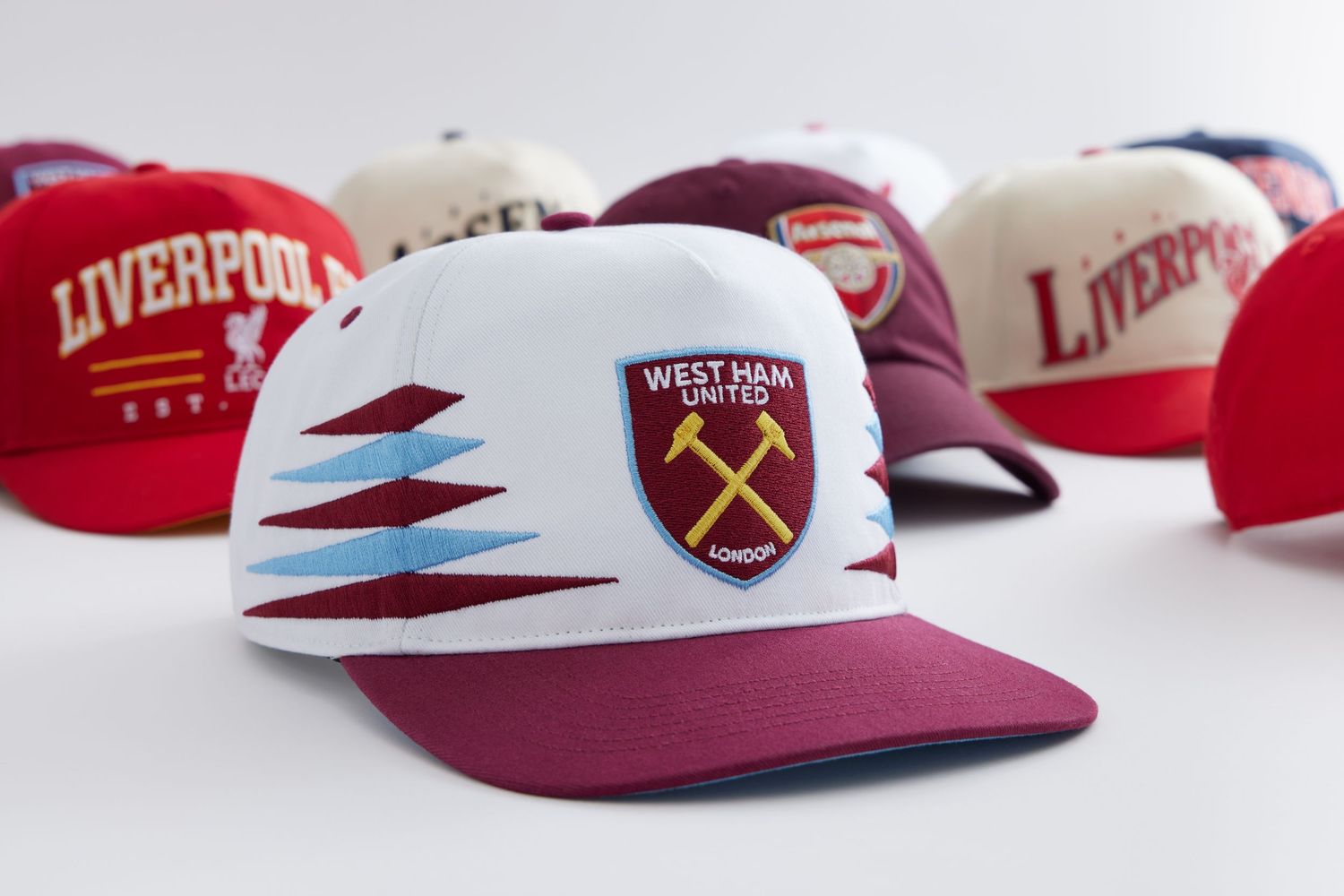 Sports team baseball caps in burgundy and white colors arranged in a row on white surface.