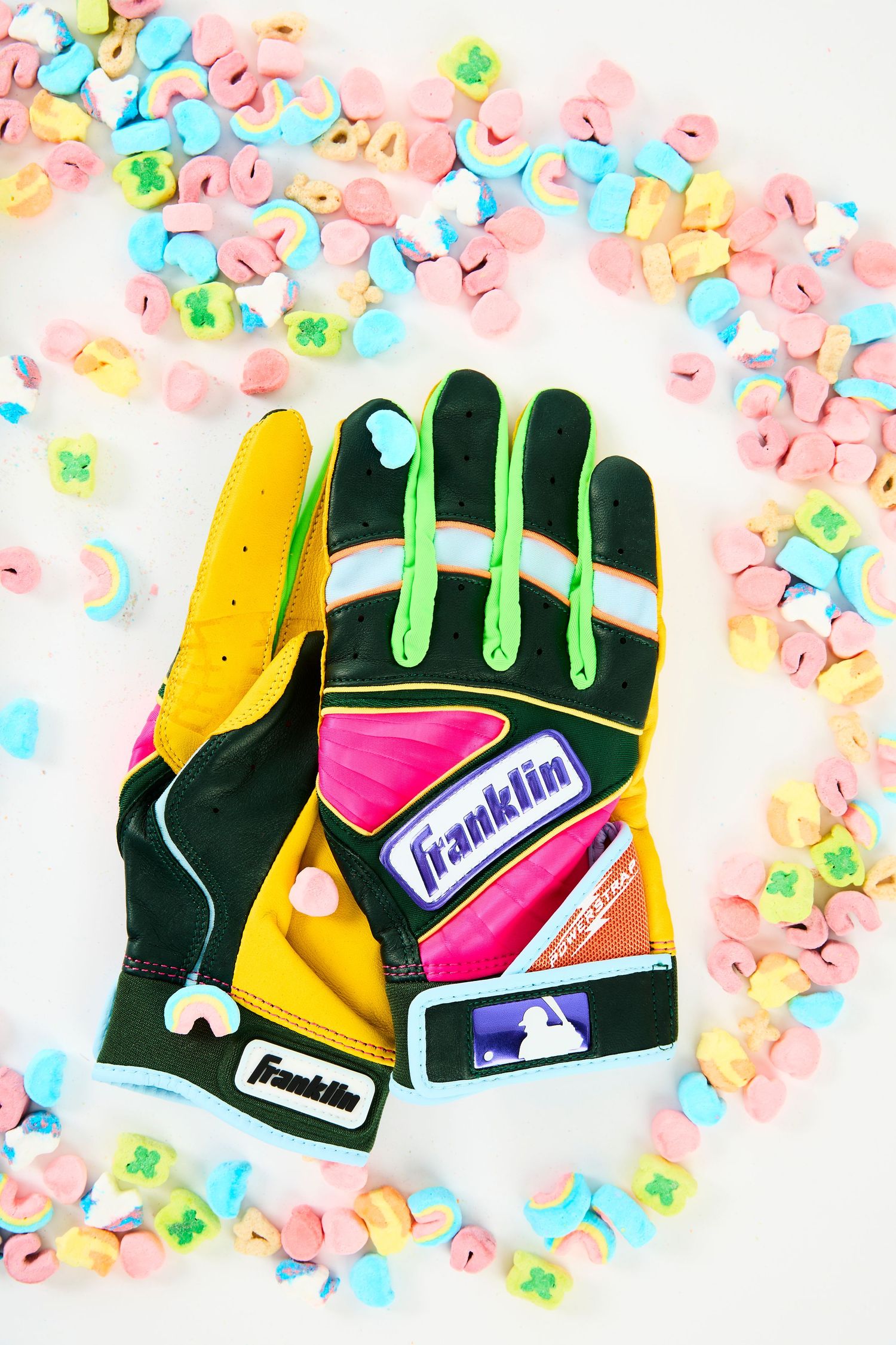 Colorful Franklin baseball batting gloves with pink and yellow accents displayed on floral confetti background.
