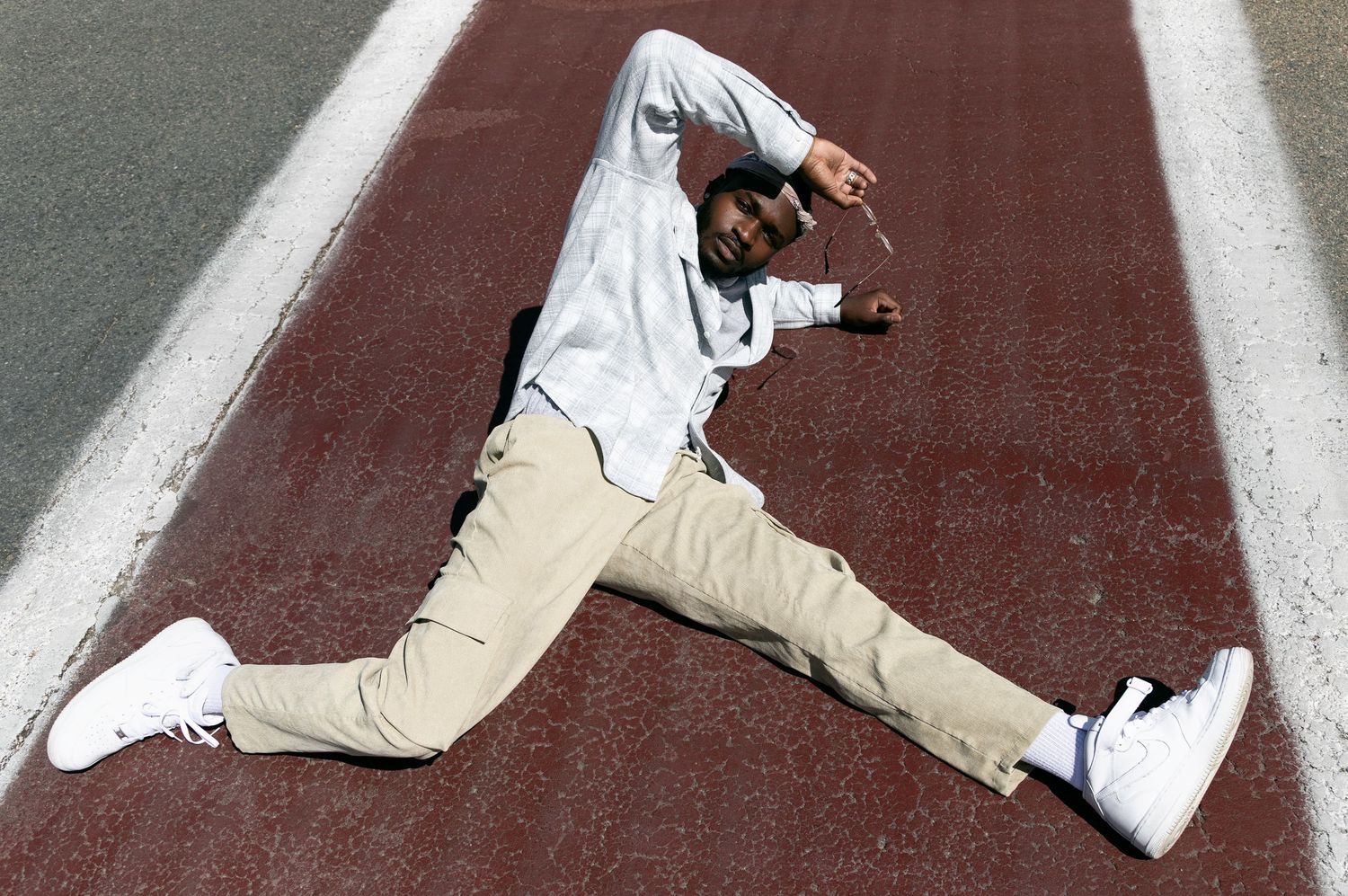 Man in beige pants and light blue, white button up shirt laying on a maroon sidewalk.