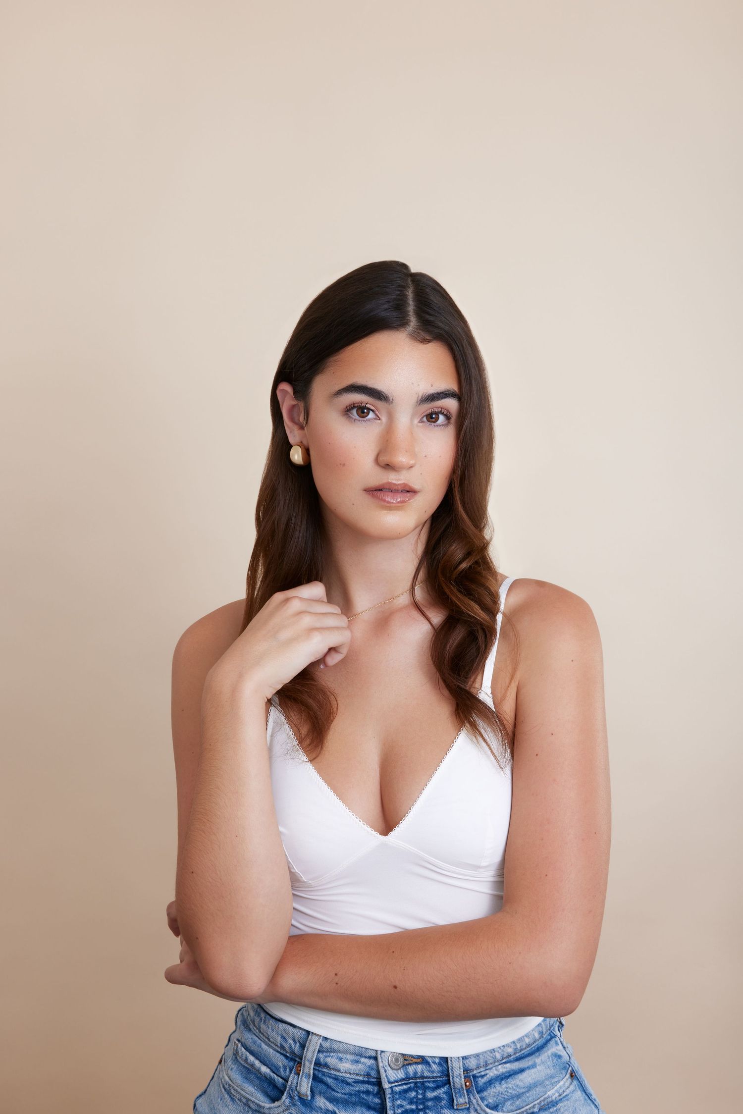 A person in a white crop top and blue jeans poses against a beige wall in a casual portrait series.