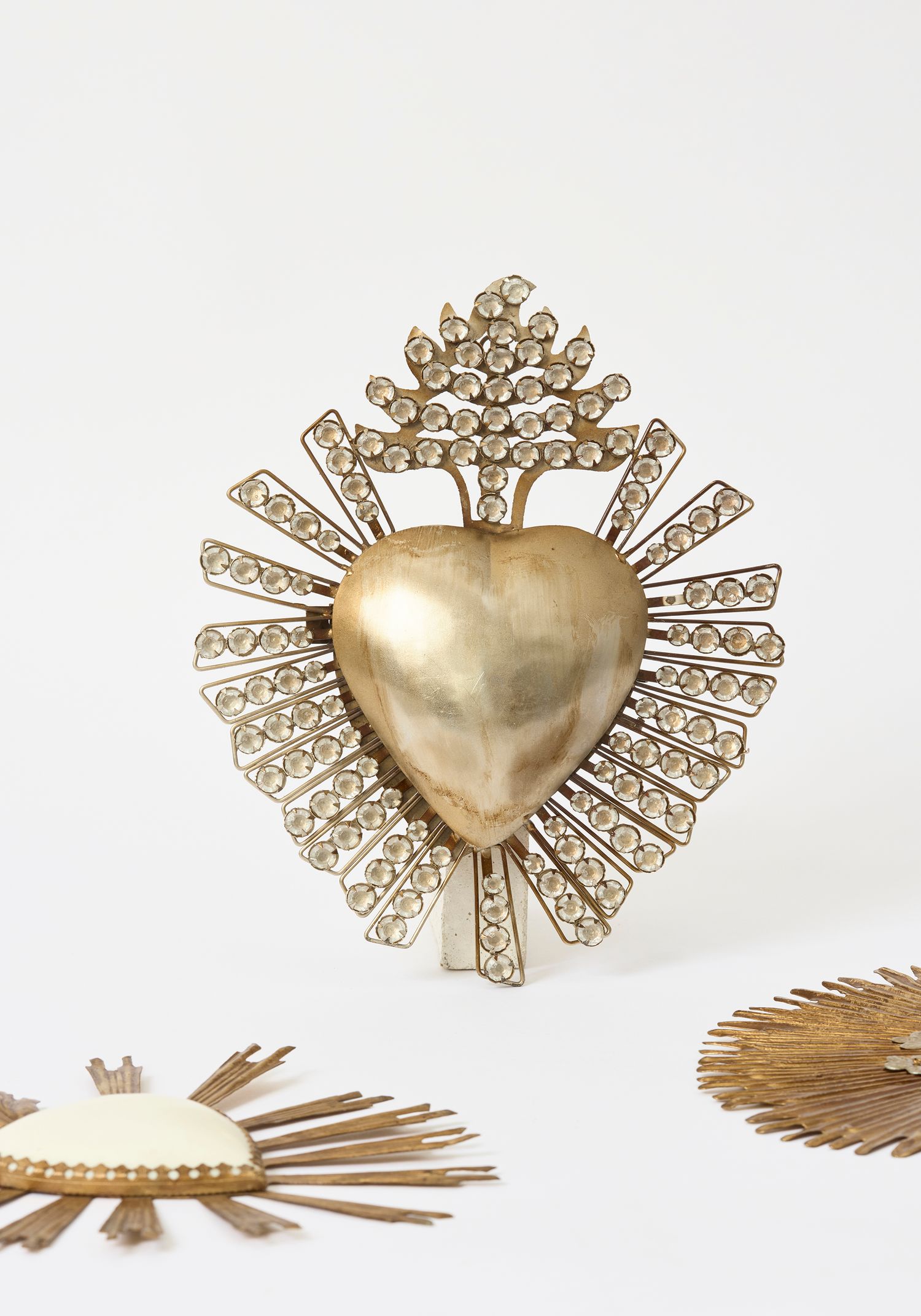 Gold sacred heart ex-voto with rhinestone rays and flames, a decorative religious artifact displayed on white background.