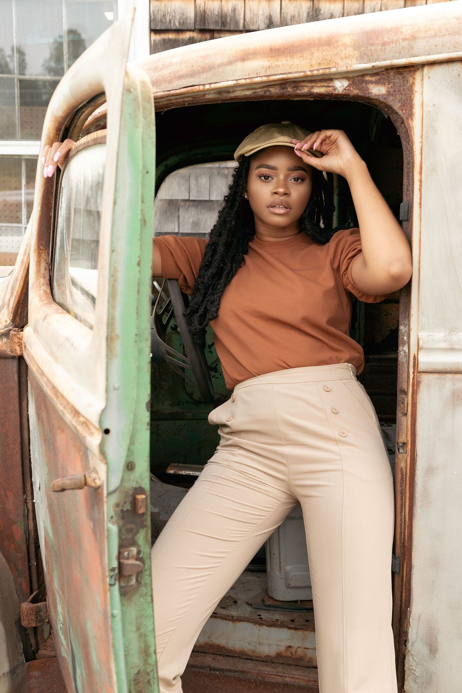 A model in brown top and beige pants poses confidently in multiple shots against a rustic backdrop with green door frame.
