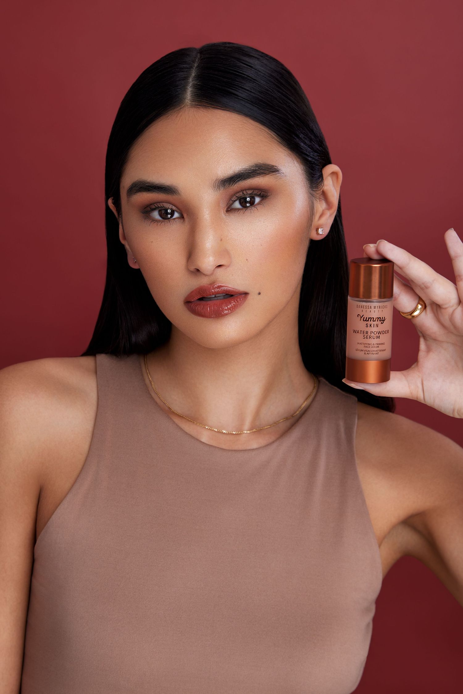 A makeup product demonstration showing bronzer application against a burgundy background.