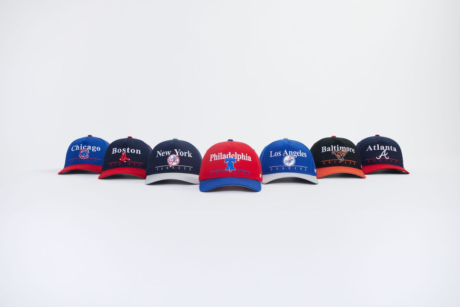 A row of sports team baseball caps including red, blue and black colors displayed on a white background.