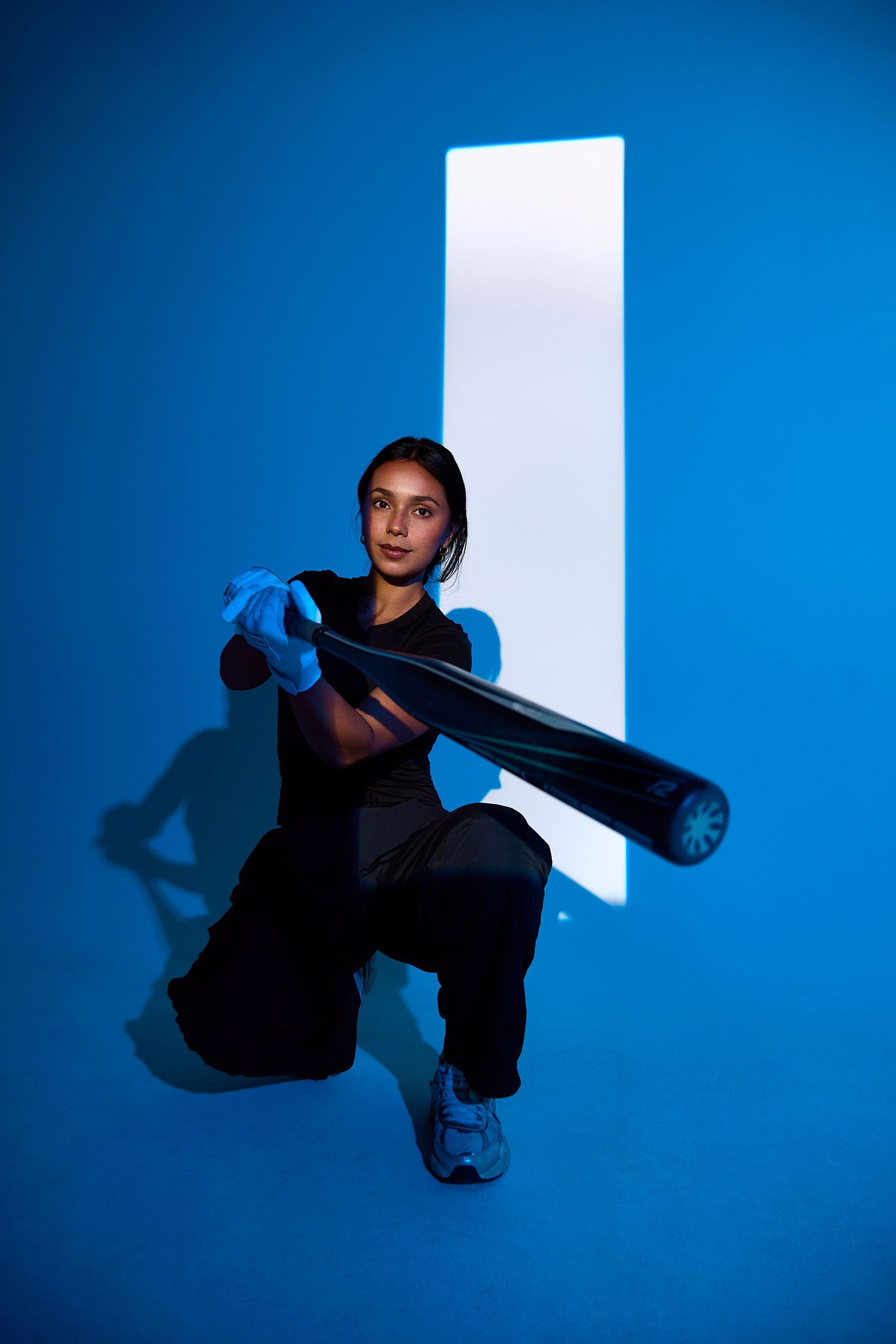 Person in black clothing crouches against blue wall creating dramatic shadows and artistic poses.