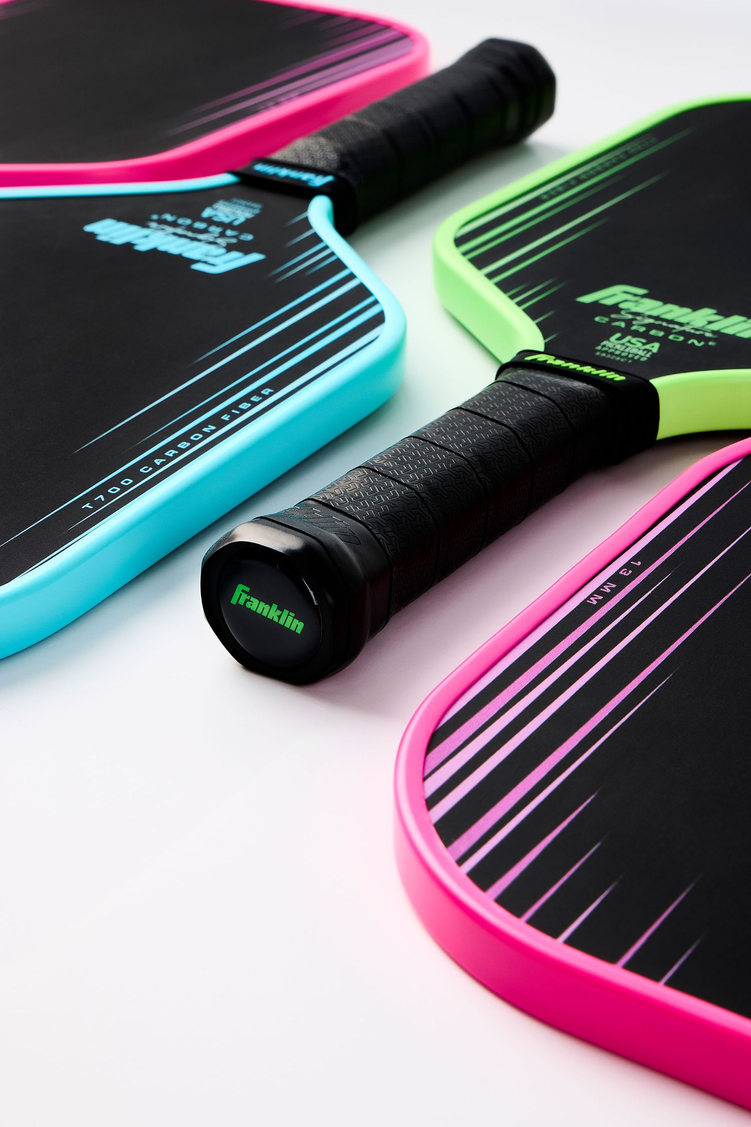 Close-up shots of colorful neon pink, blue and green Franklin pickleball paddles against black background.