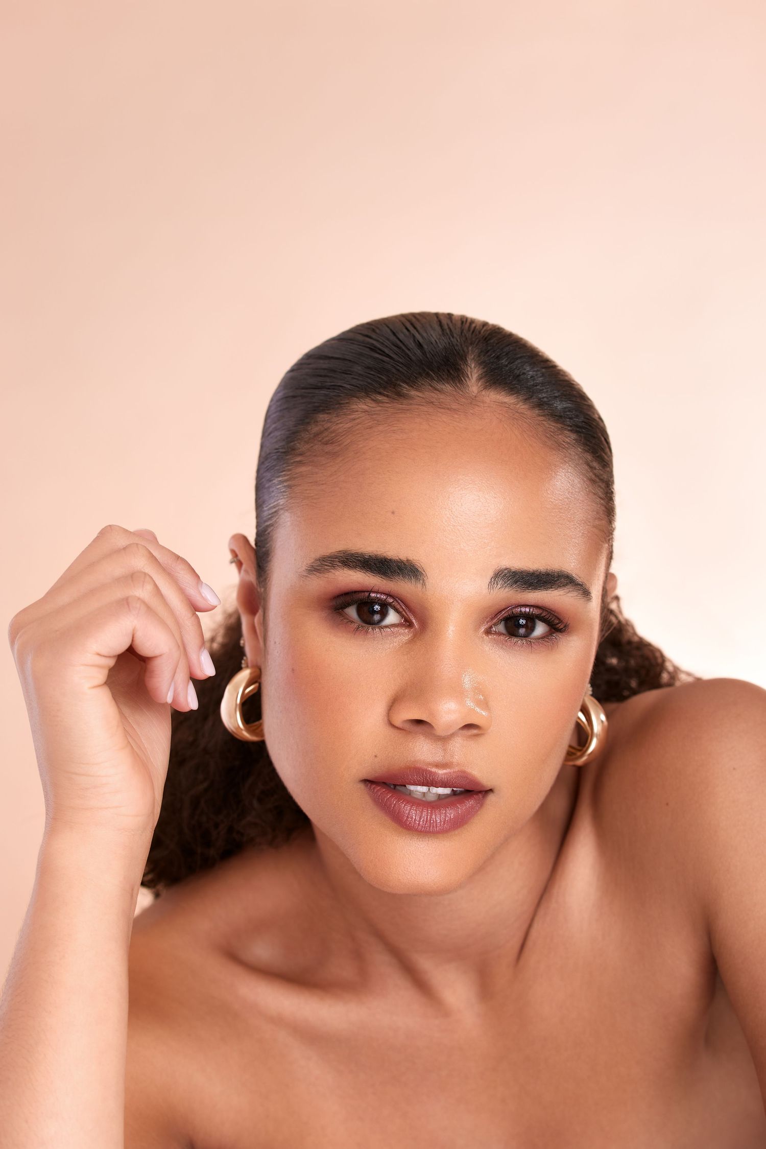 Beauty portrait with glowing skin and neutral makeup against pink background.