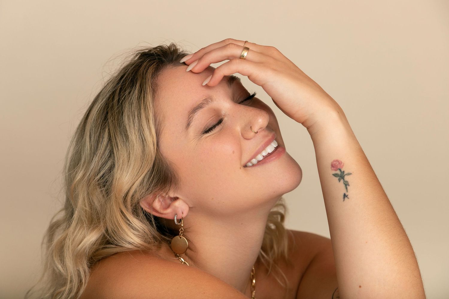 A joyful expression and gentle hand gesture shown in a warm-toned portrait with a visible star tattoo on the arm.