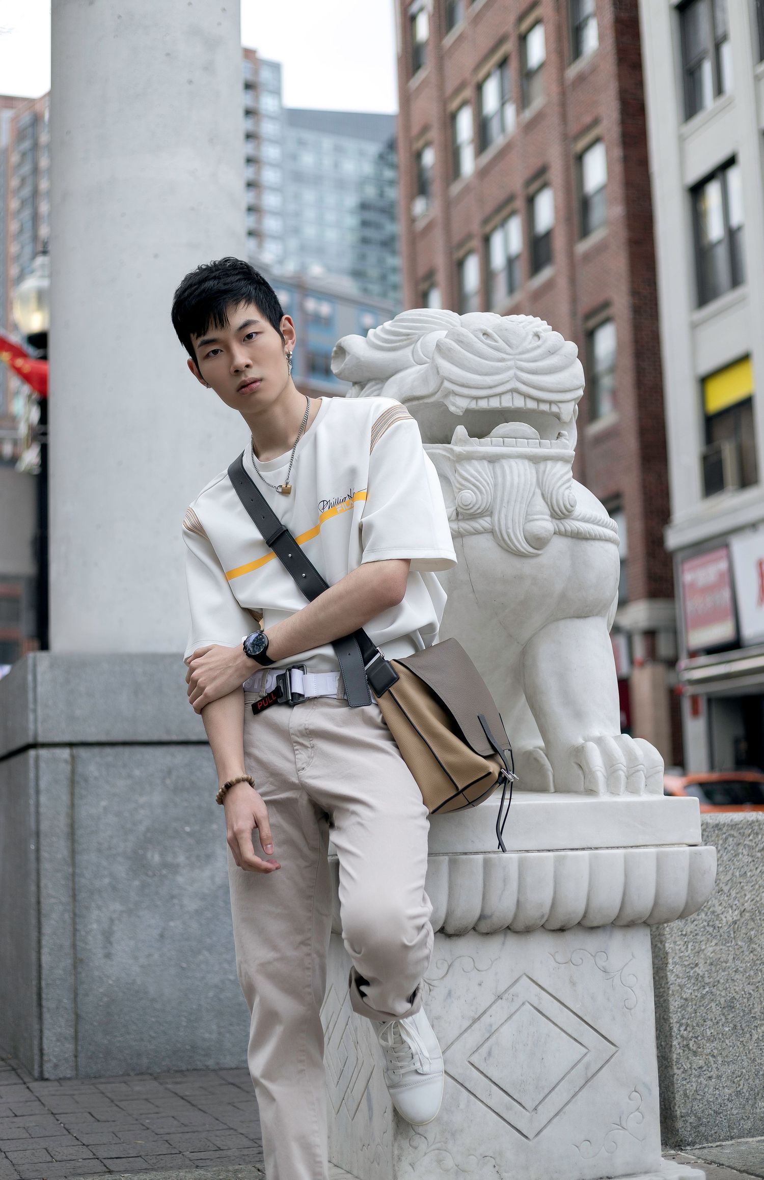 A person in casual white and beige attire poses with a decorative stone lion statue in an urban setting.