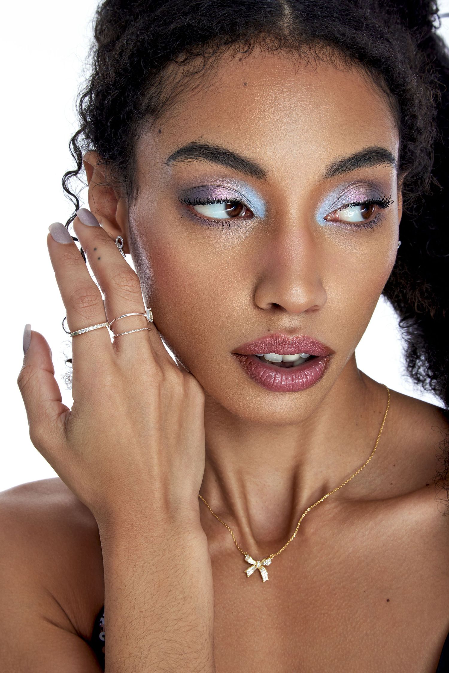 Beauty portrait showcasing delicate jewelry and glamorous purple eyeshadow makeup with glossy mauve lips.