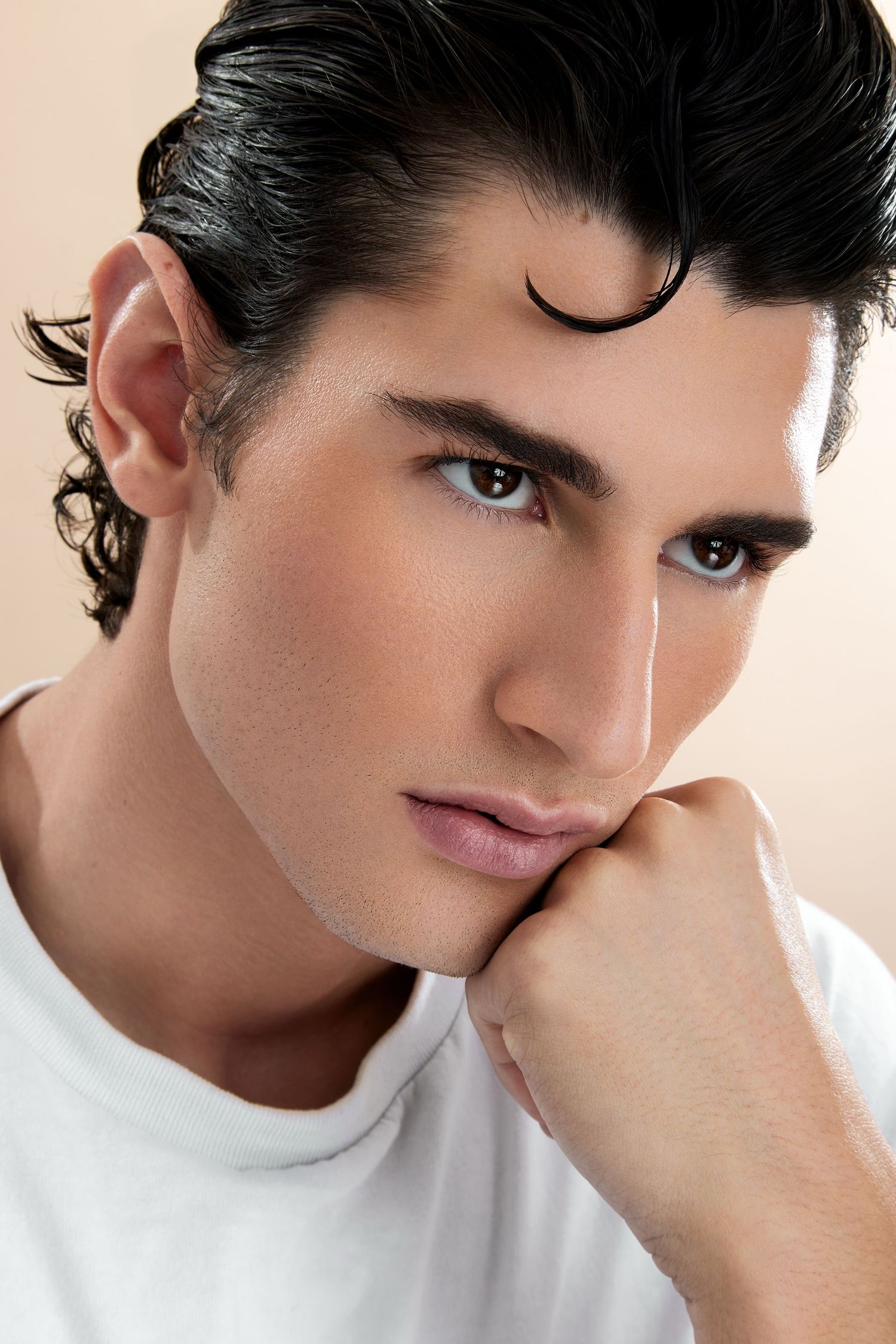 Close-up beauty portrait of a model with dark styled hair wearing a white t-shirt against neutral background.