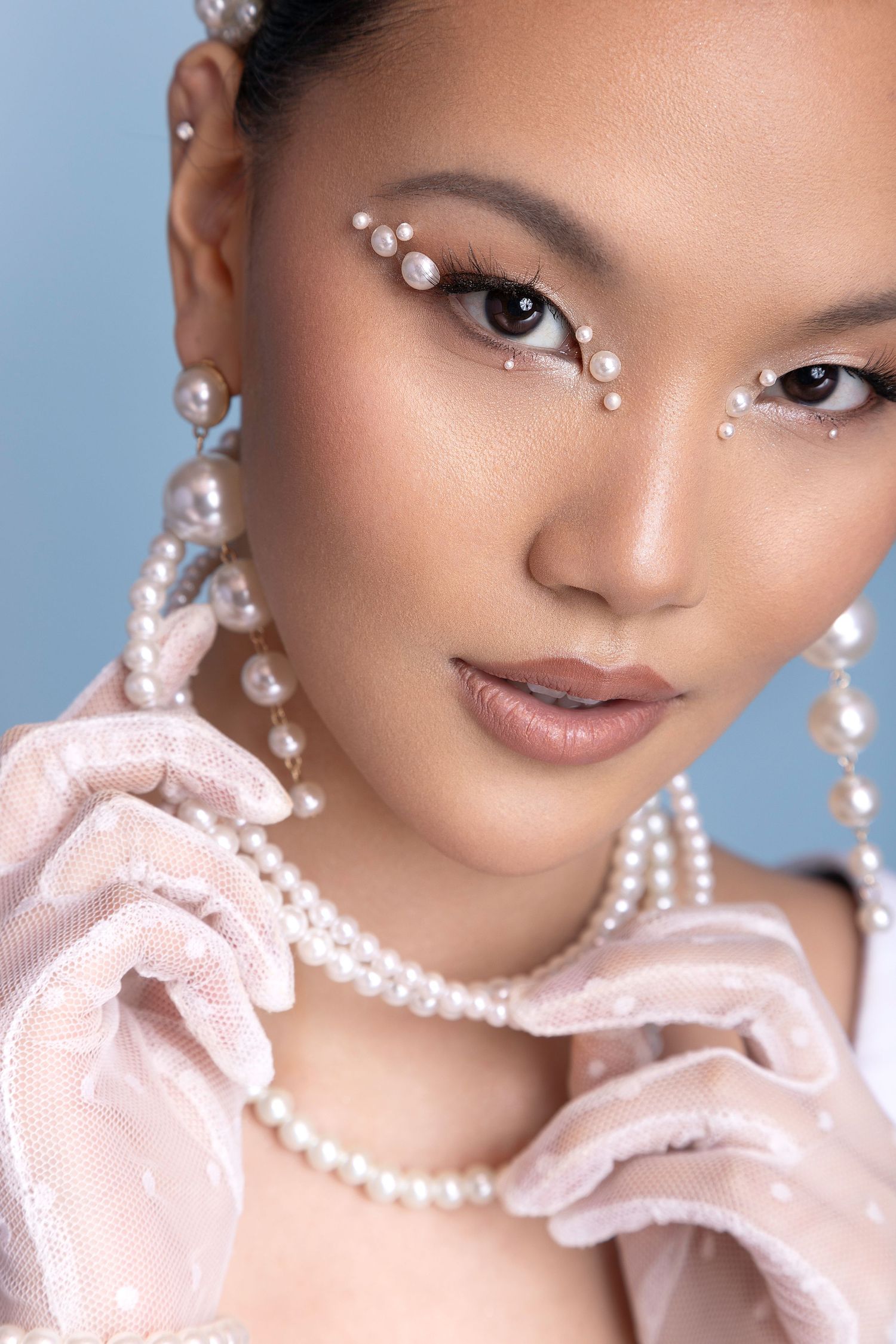 Beauty portrait with delicate pearl details and soft pink ruffled collar against blue background.