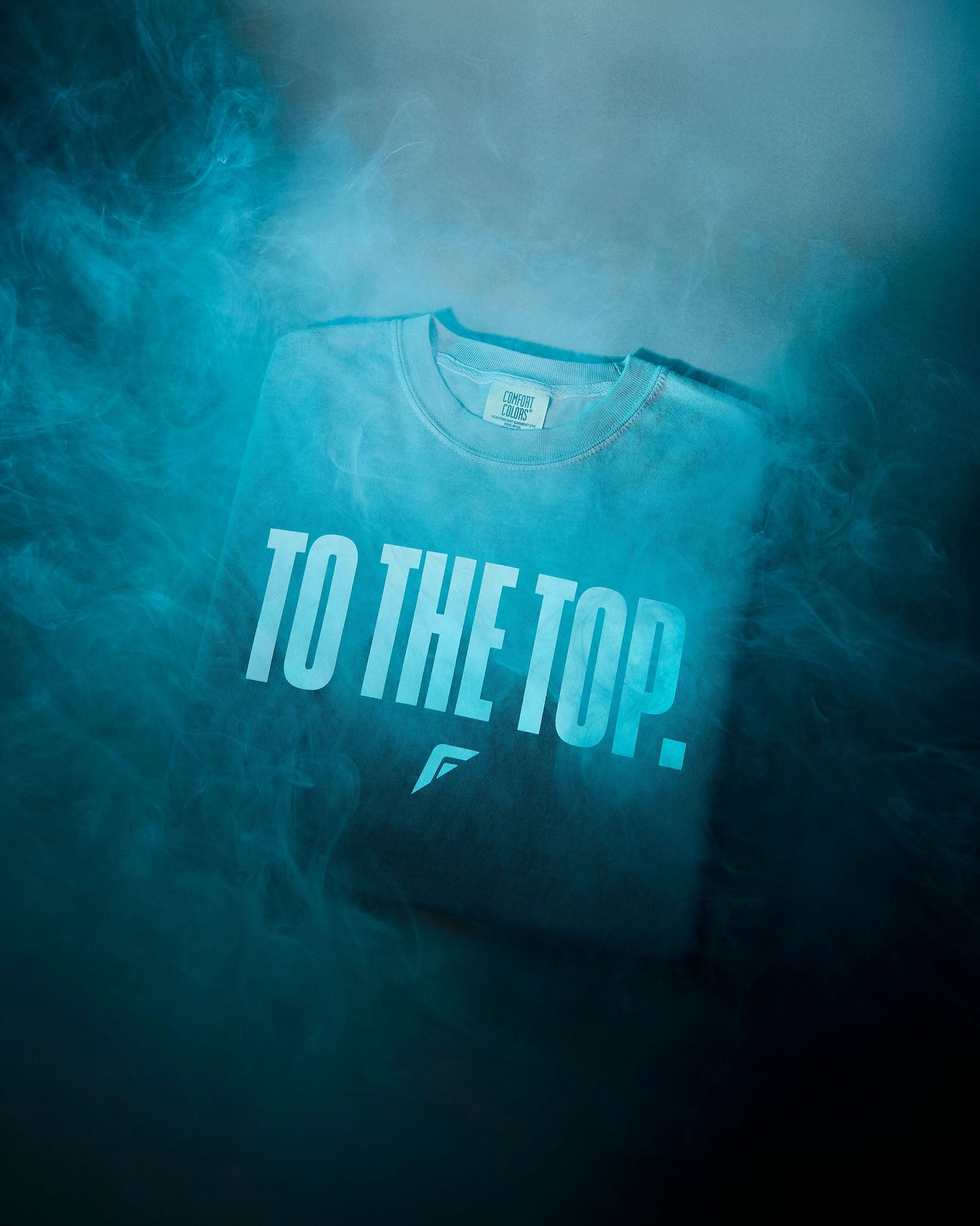 A series of dark teal colored t-shirts photographed in moody lighting with 'To The Top' text visible on them.