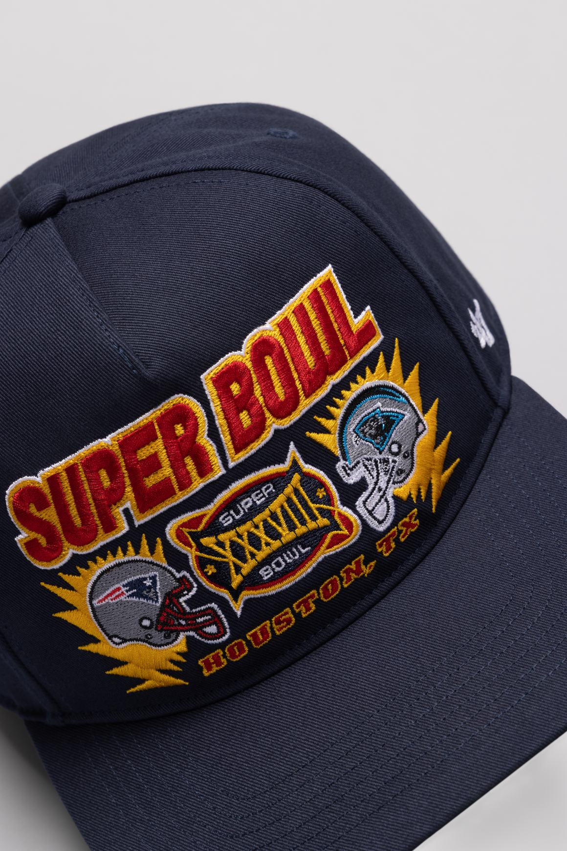 A navy blue baseball cap with Super Bowl XXXVIII logo patch featuring the Patriots and Panthers team emblems.