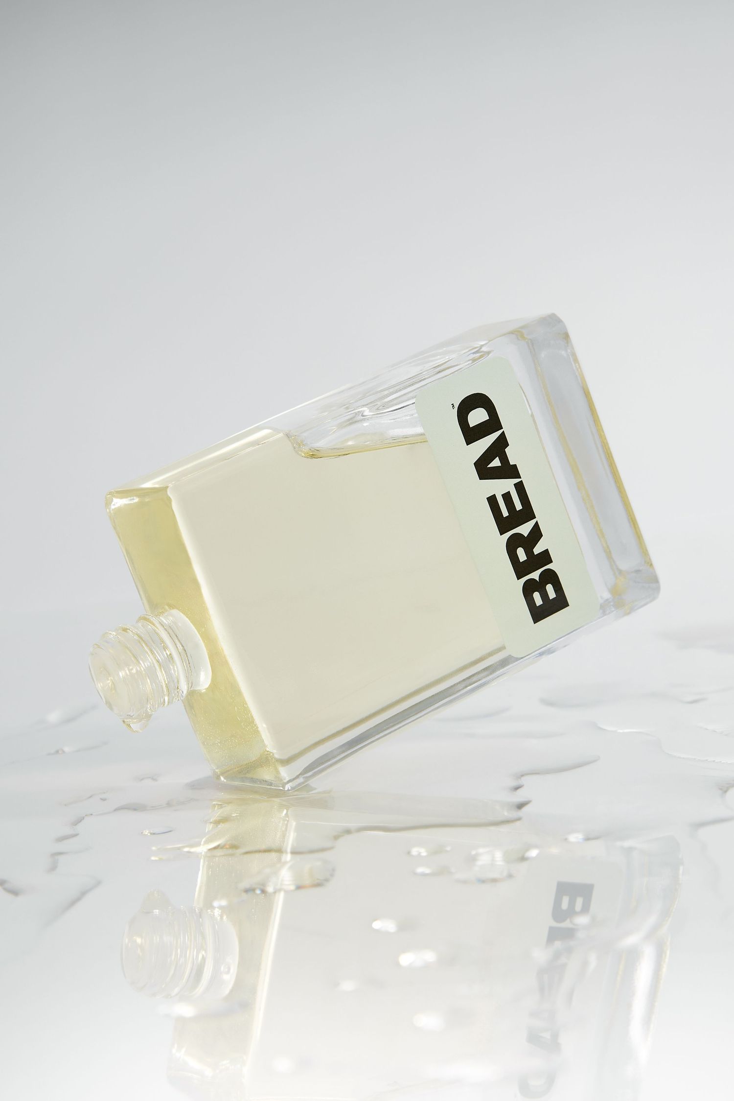 Clear glass perfume bottles labeled 'BREAD' arranged at dynamic angles on reflective surface.