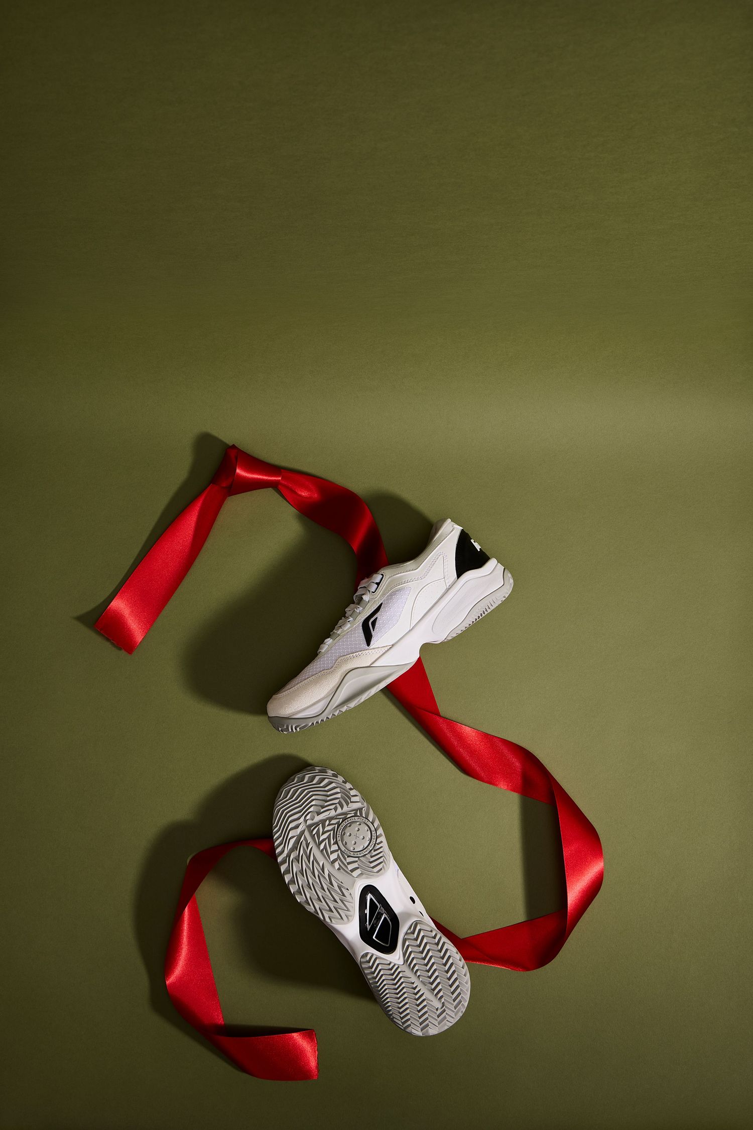 White Nike sneakers with flowing red ribbon against green background create artistic composition.