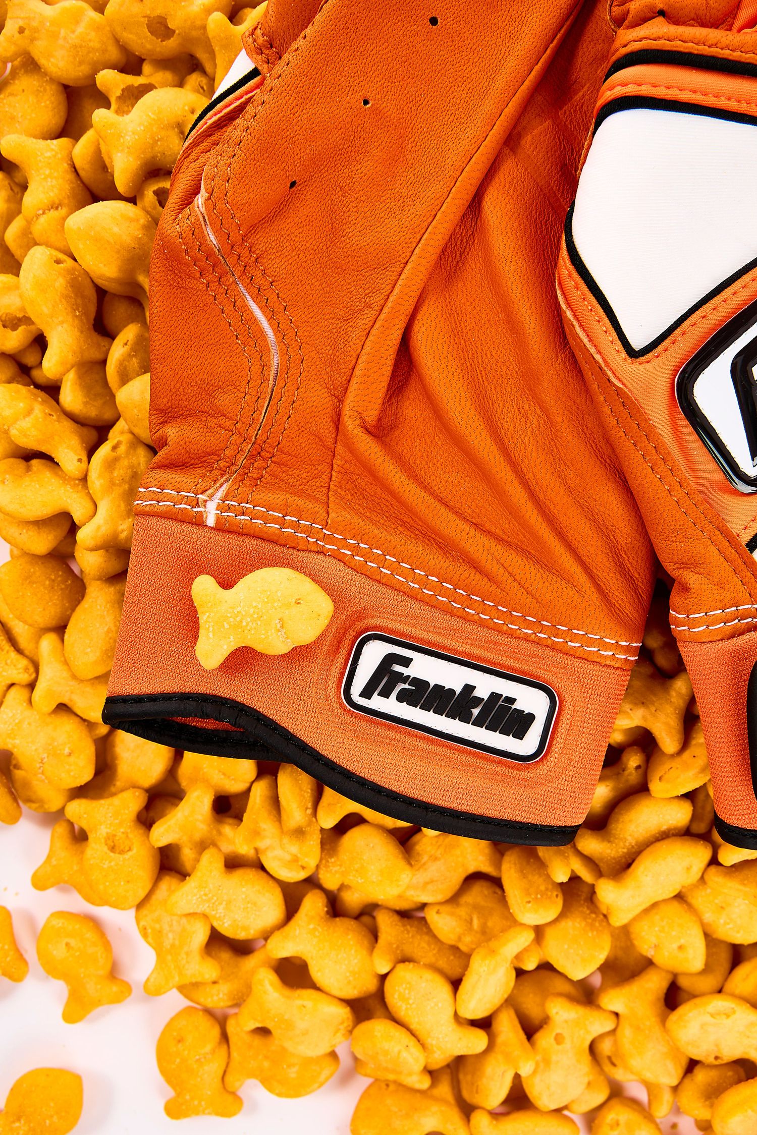 Orange baseball glove surrounded by scattered goldfish crackers on white background.