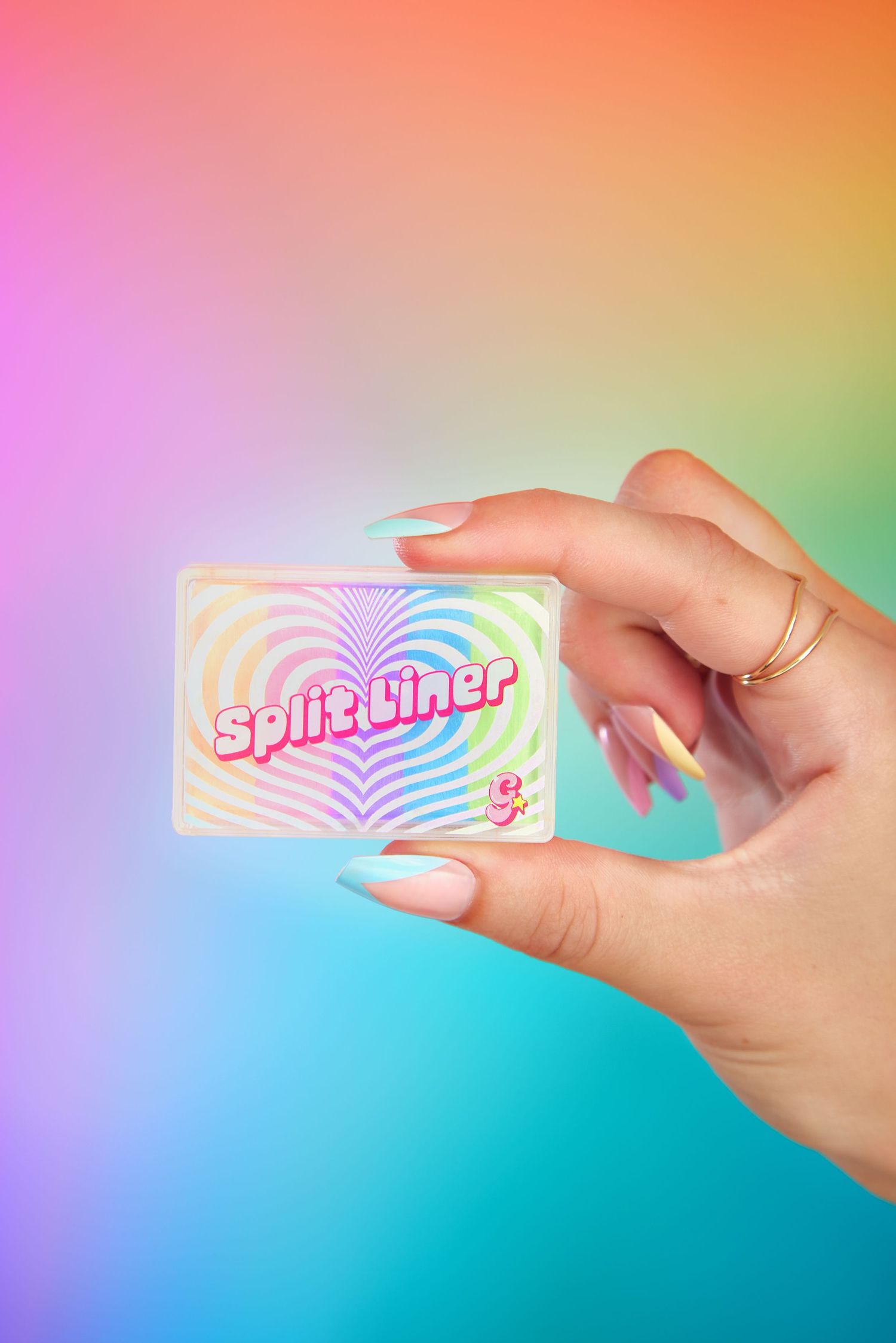 A hand holds a holographic sticker against a colorful gradient background with pink, orange and teal tones.