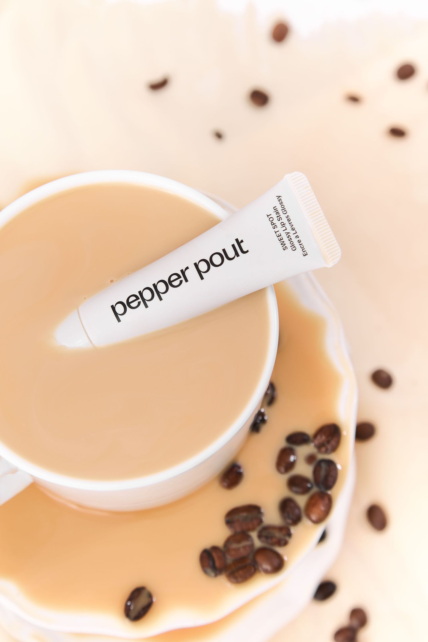 Pepper Pout lip plumper tube resting on a coffee cup with scattered coffee beans on a light background.
