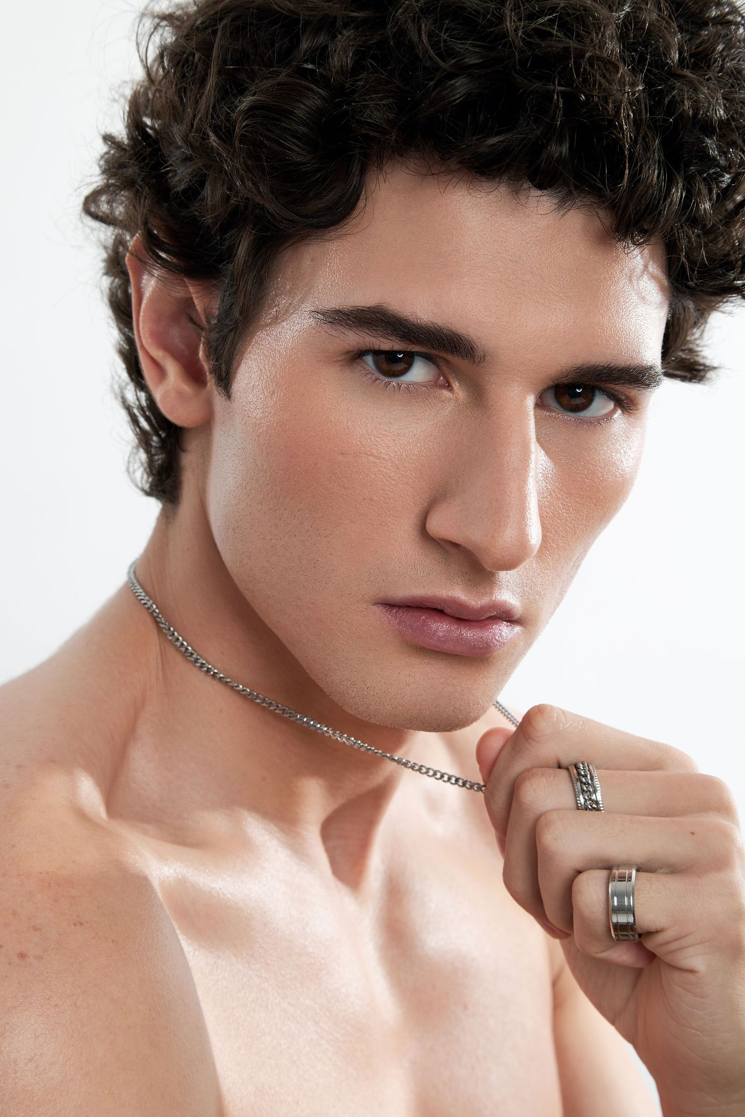 Close-up fashion portrait showing silver chain necklace and ring accessories against bare shoulders.