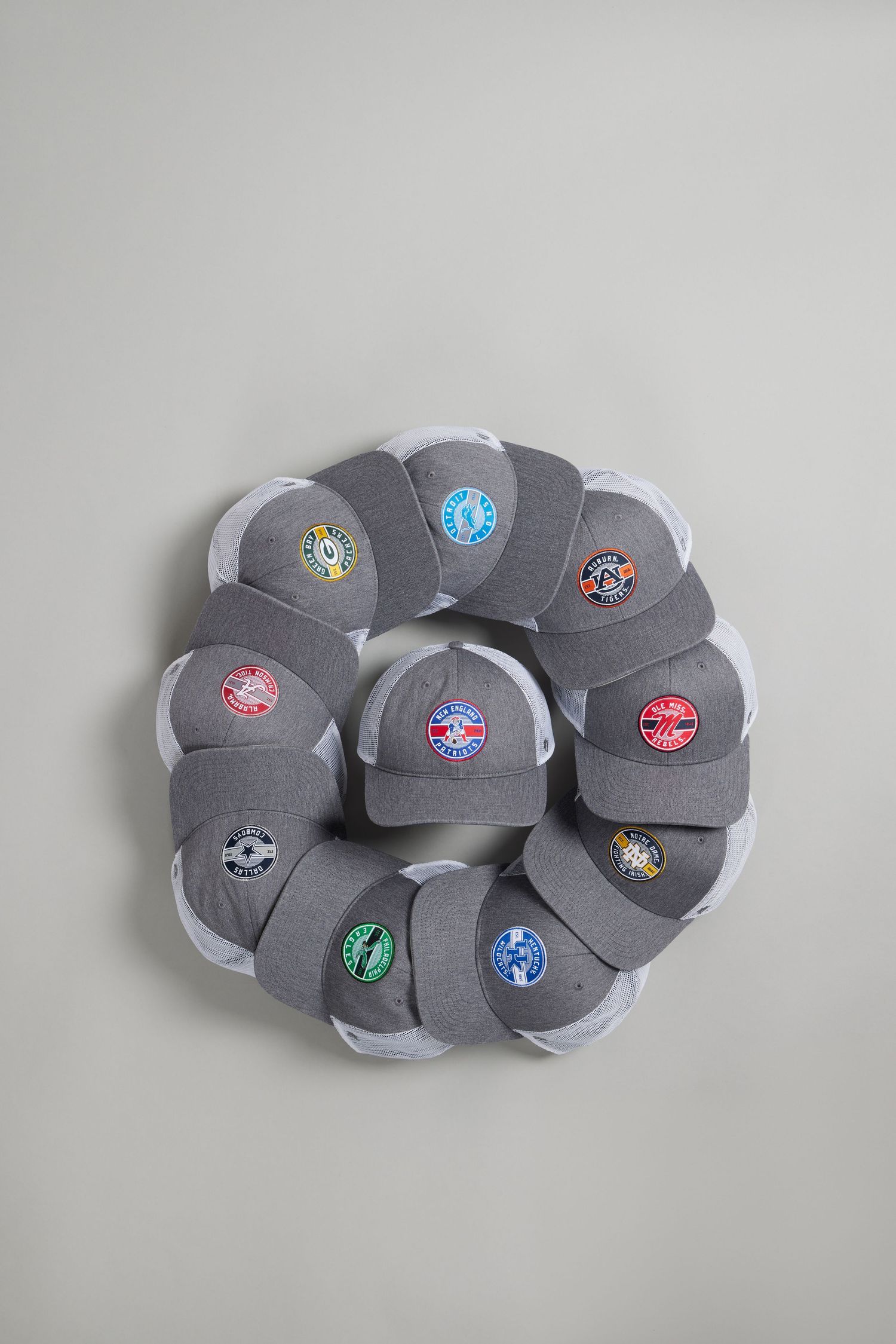 Collection of grey baseball caps with various sports team logos arranged in circular pattern.