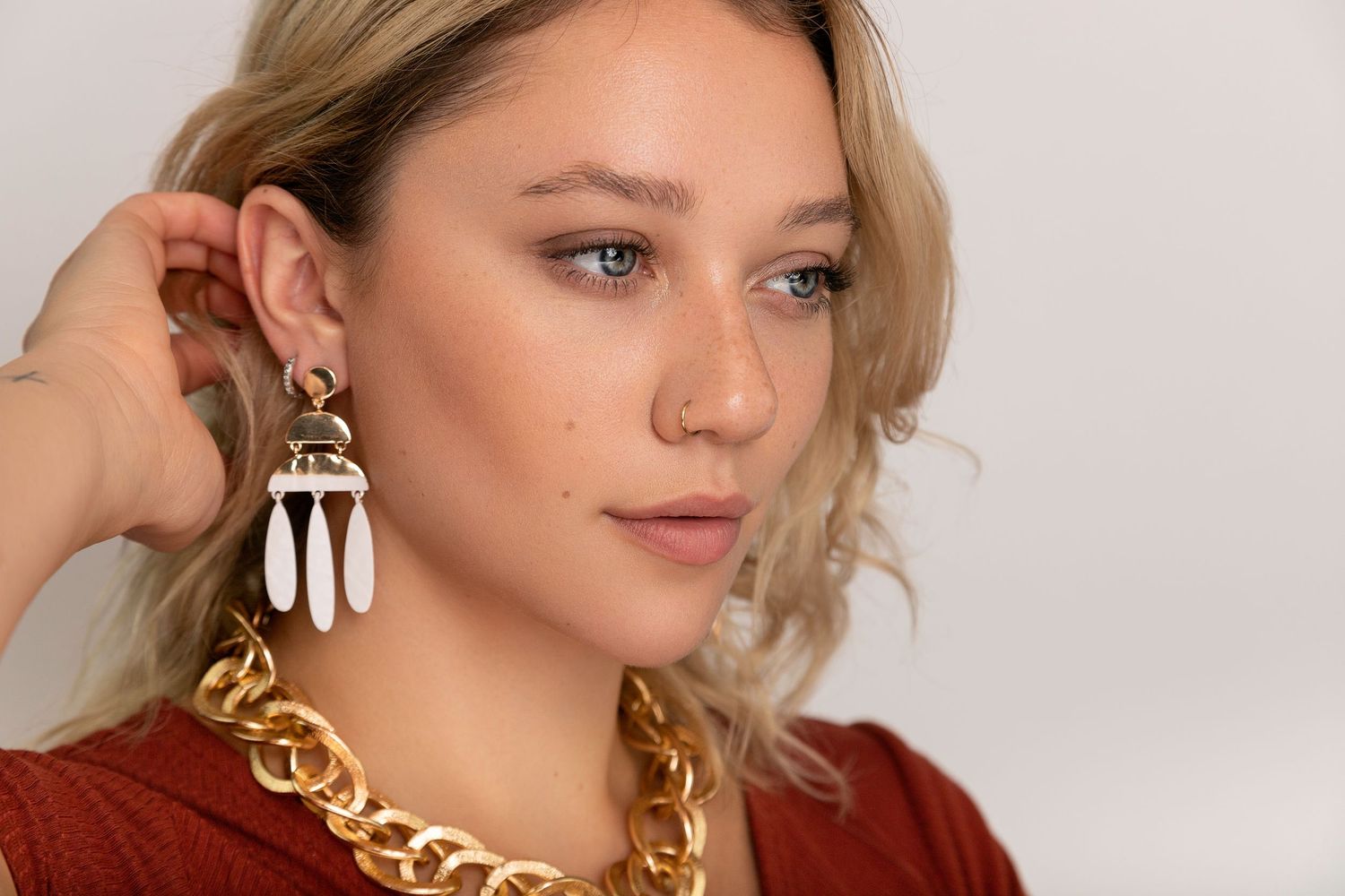 Woman in gold chain necklace and statement earrings poses against neutral background.