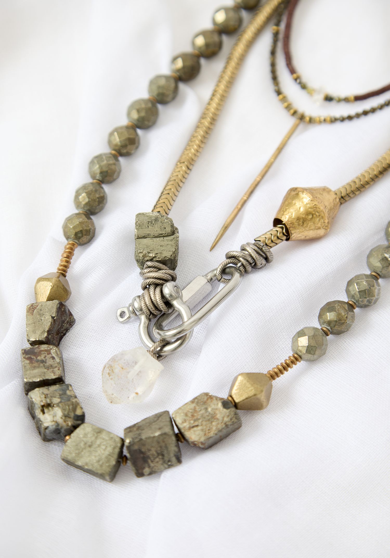 Layered pyrite and gold beaded necklaces with silver clasp on white fabric background.