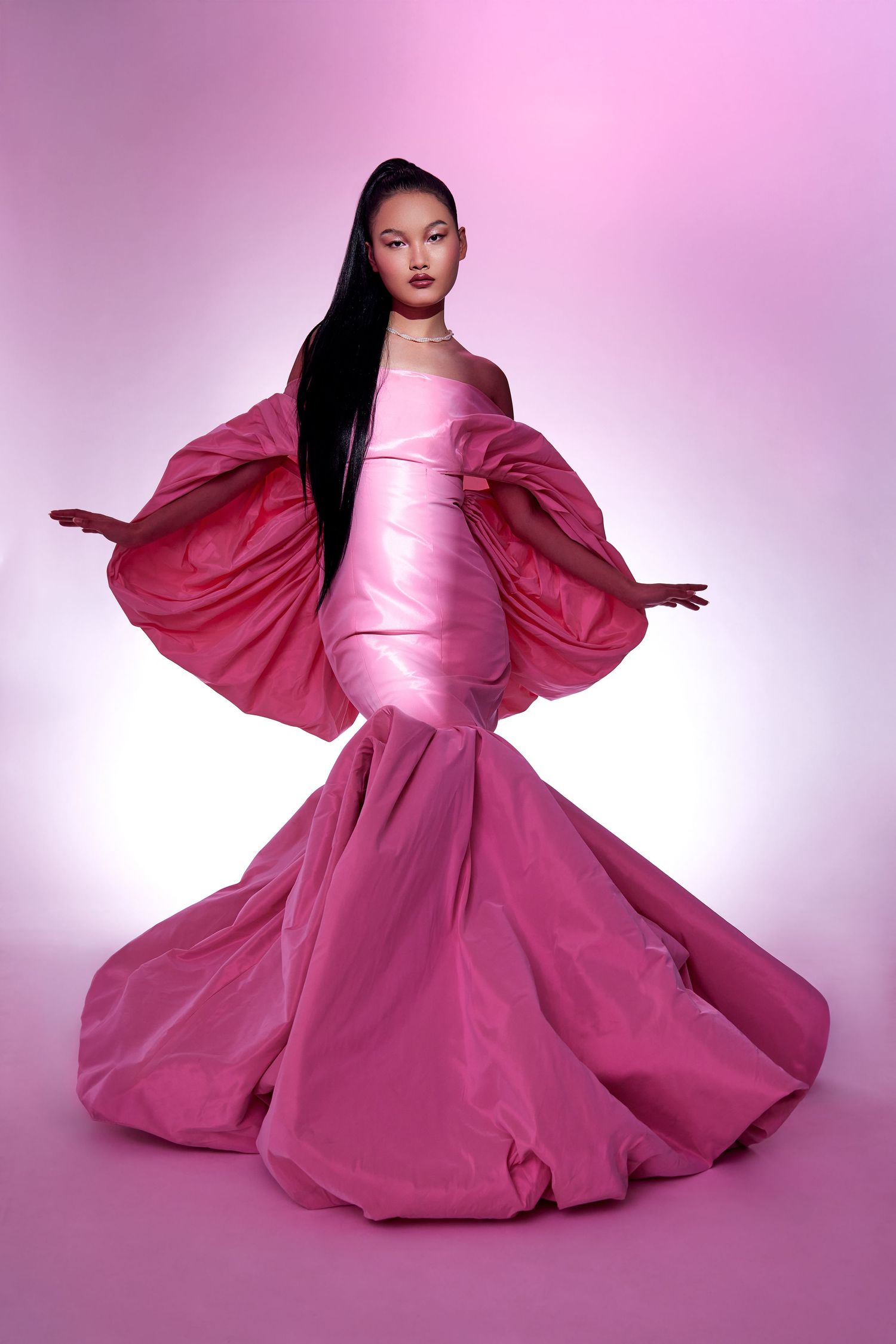 Fashion model poses in flowing pink gown with dramatic balloon sleeves against gradient background.