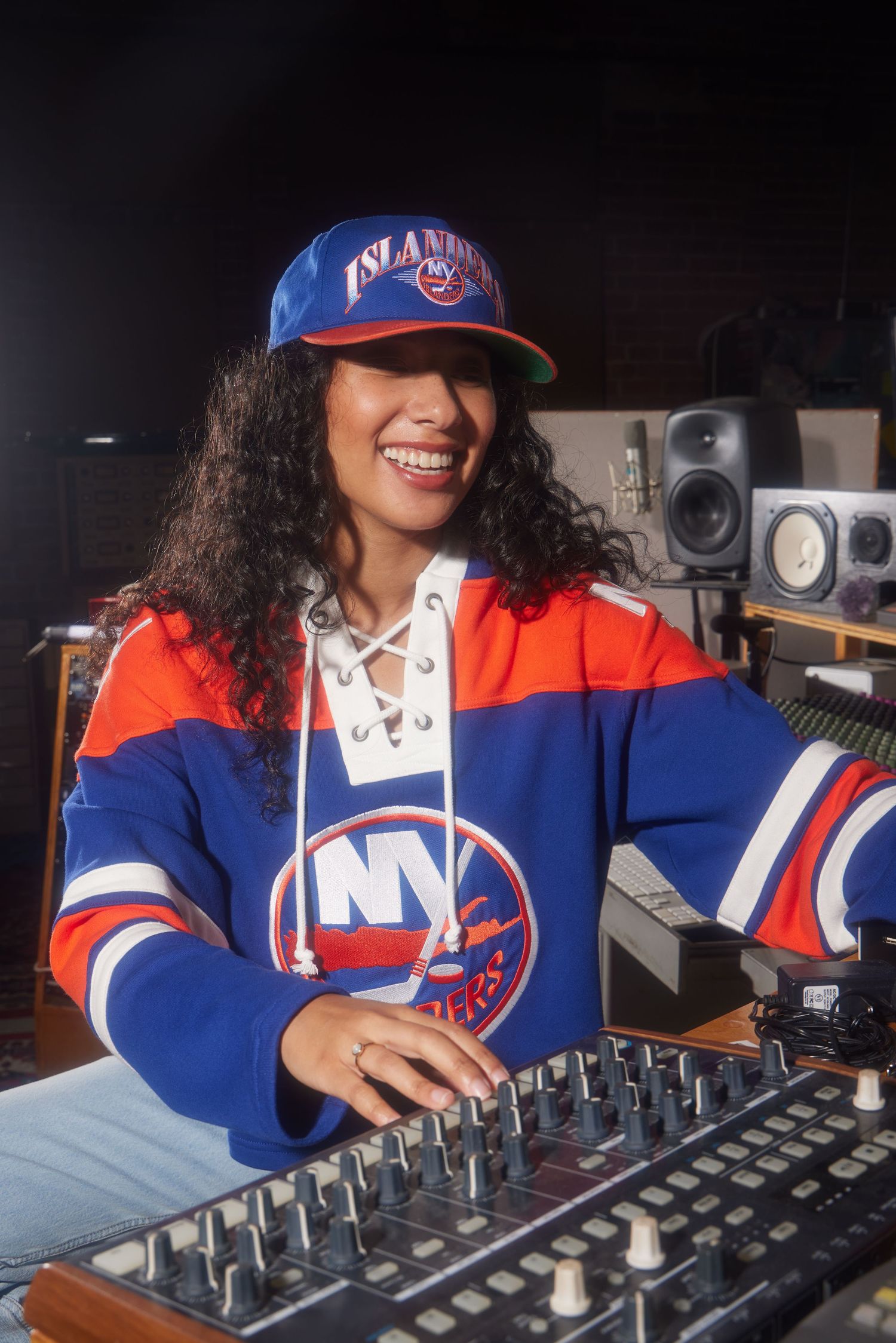DJ wearing New York Islanders hockey jersey works at mixing board console in recording studio.