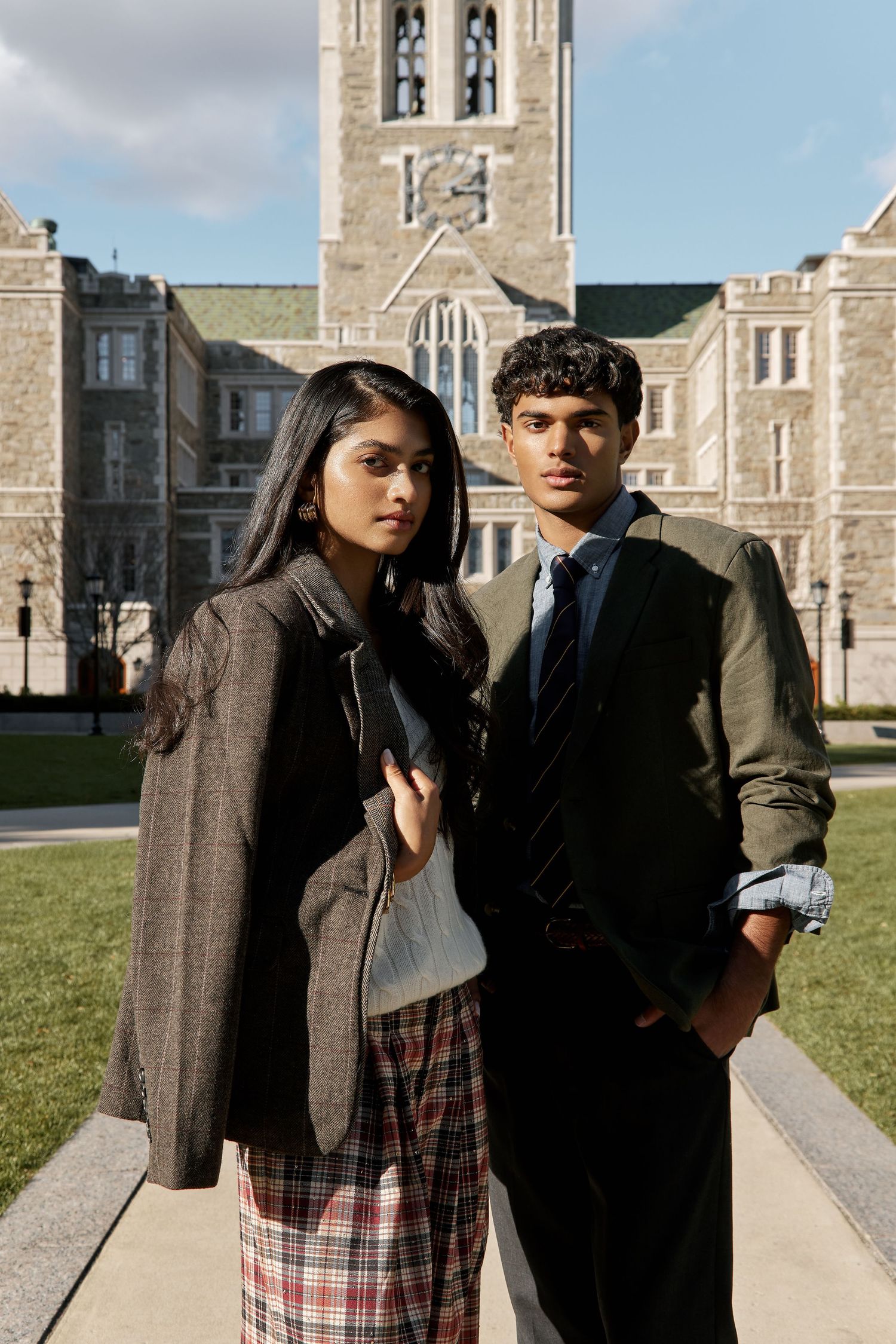 Two people in casual attire pose together in front of a stone building with Gothic architecture.