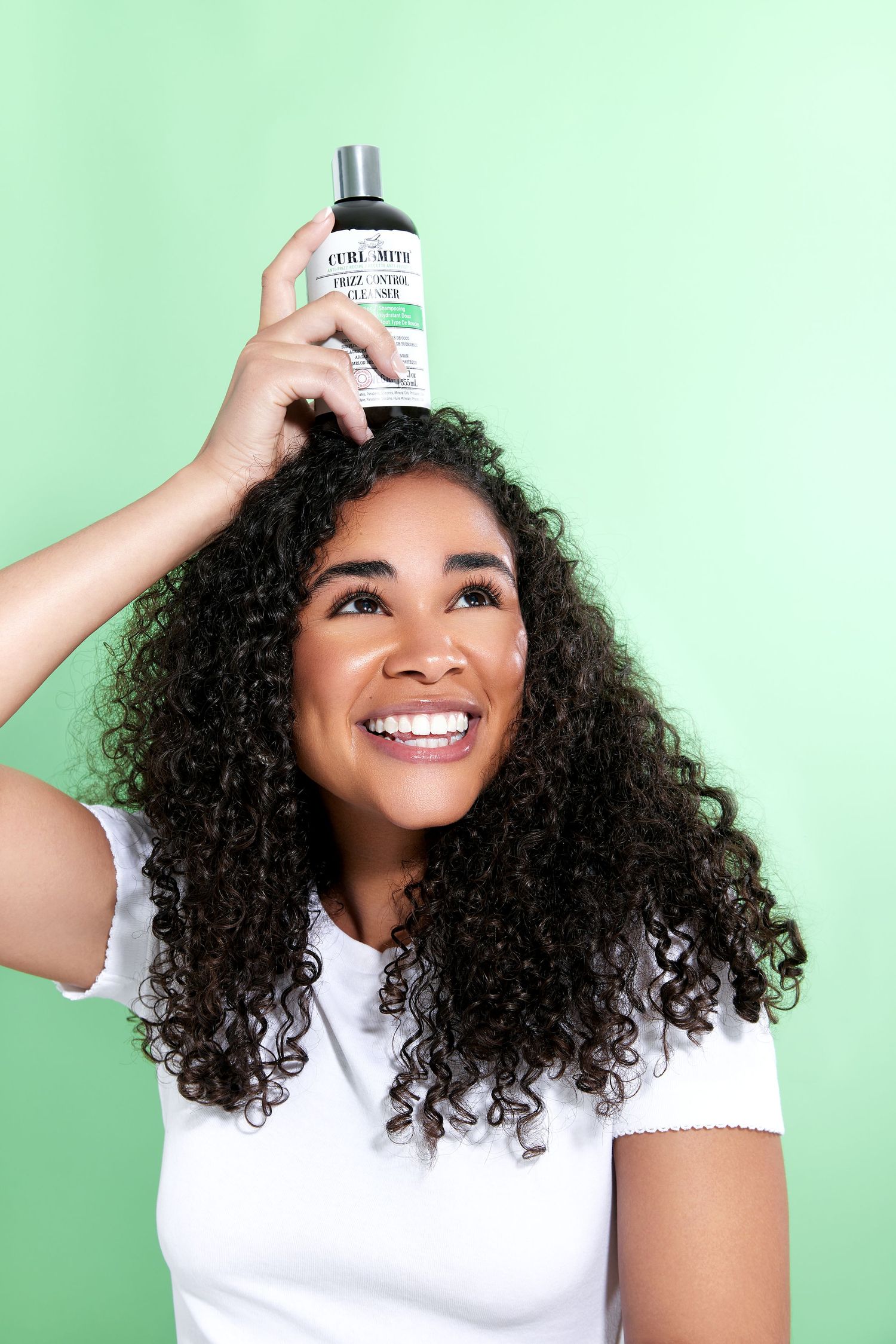A series of photos showing someone applying hair oil to their curly hair against a mint green background.