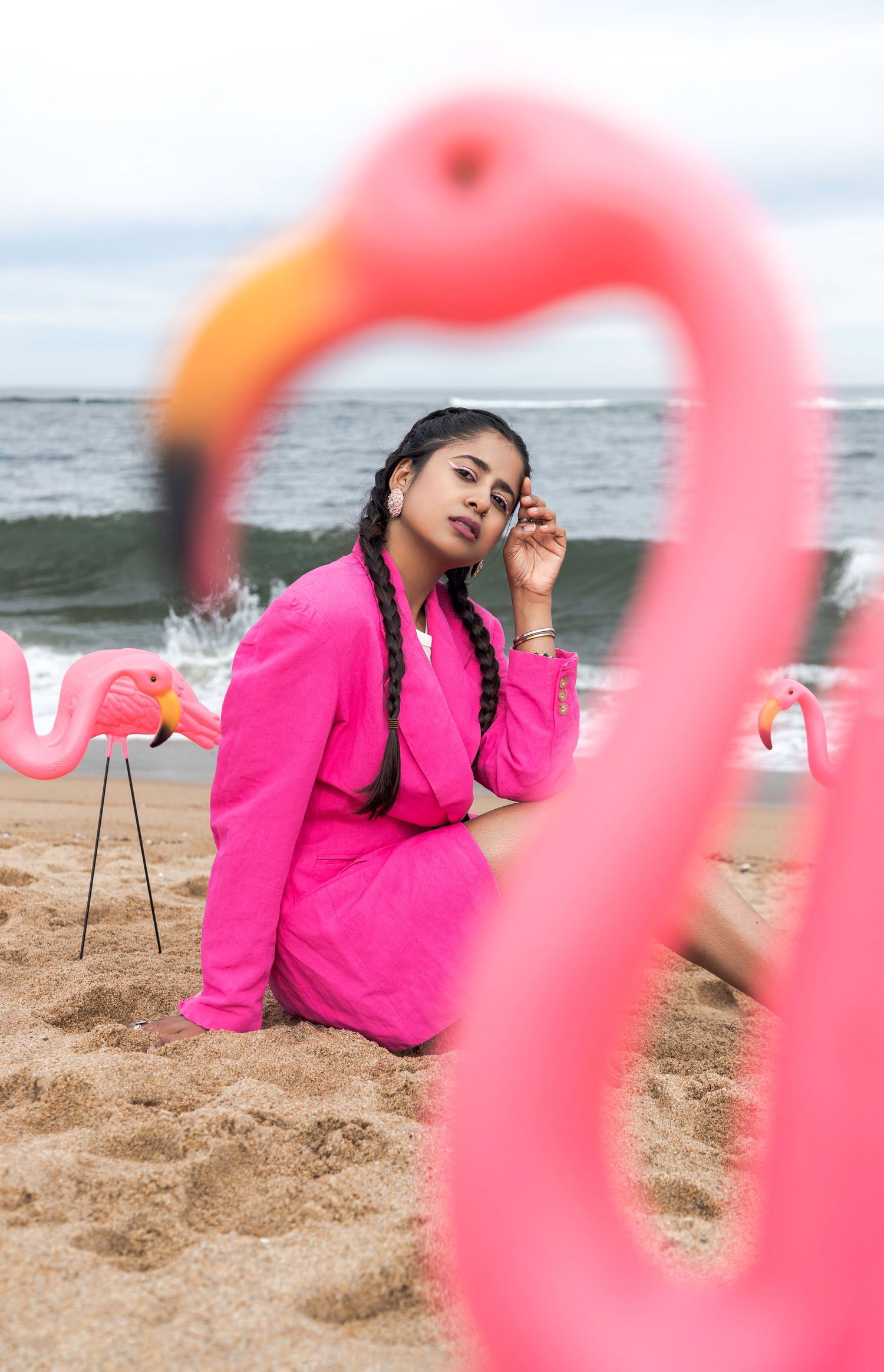 Person in bright pink blazer poses on sandy beach with pink flamingo pool float in foreground.