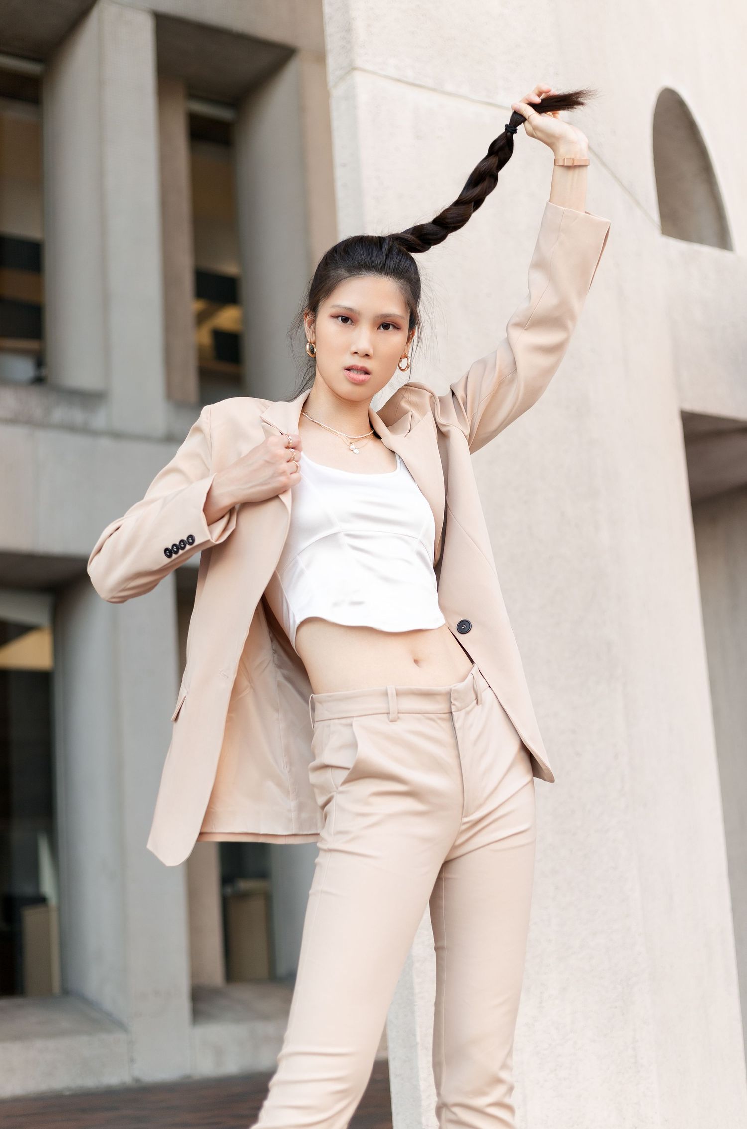 Woman in a beige pantsuit and white crop top strikes dynamic poses in an architectural setting.