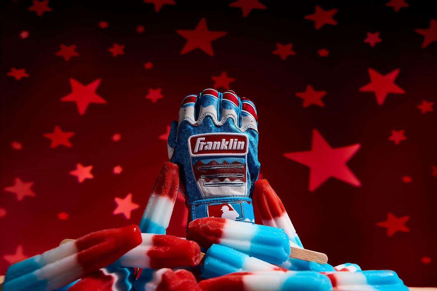A pair of blue and gray Franklin brand batting gloves against a red starry background.