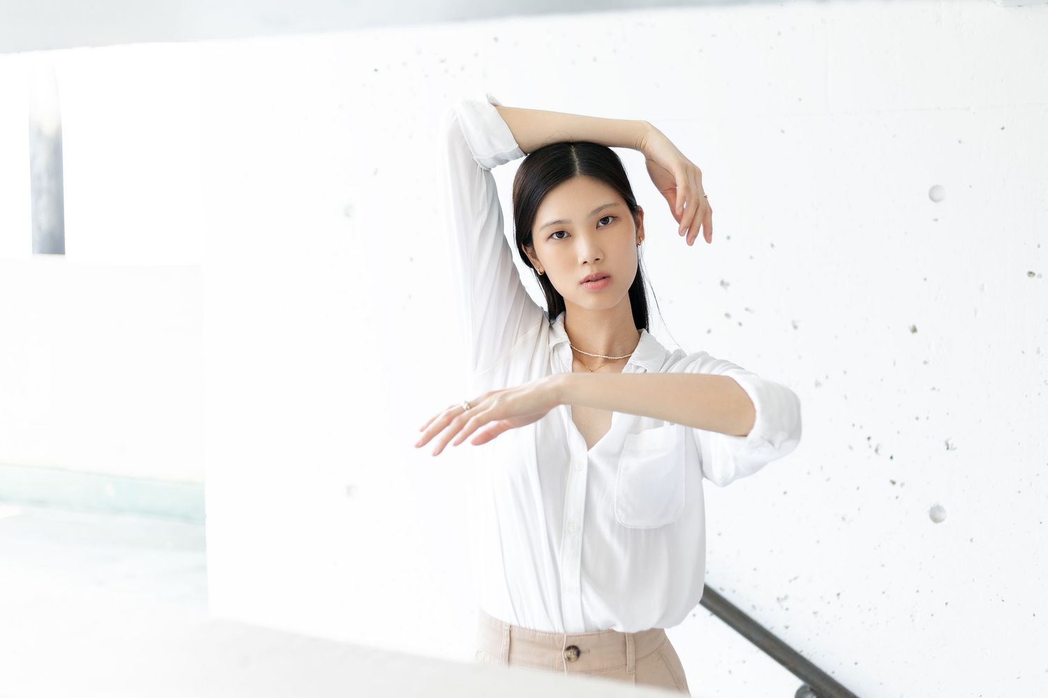 Woman in white outfit poses gracefully against white background framing her face with graceful movements.