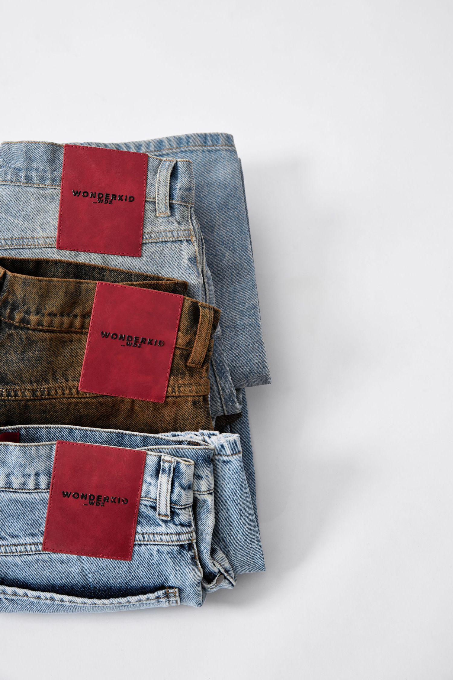 Three folded Wonderkid jeans stacked, featuring light blue and brown denim styles with red brand labels.